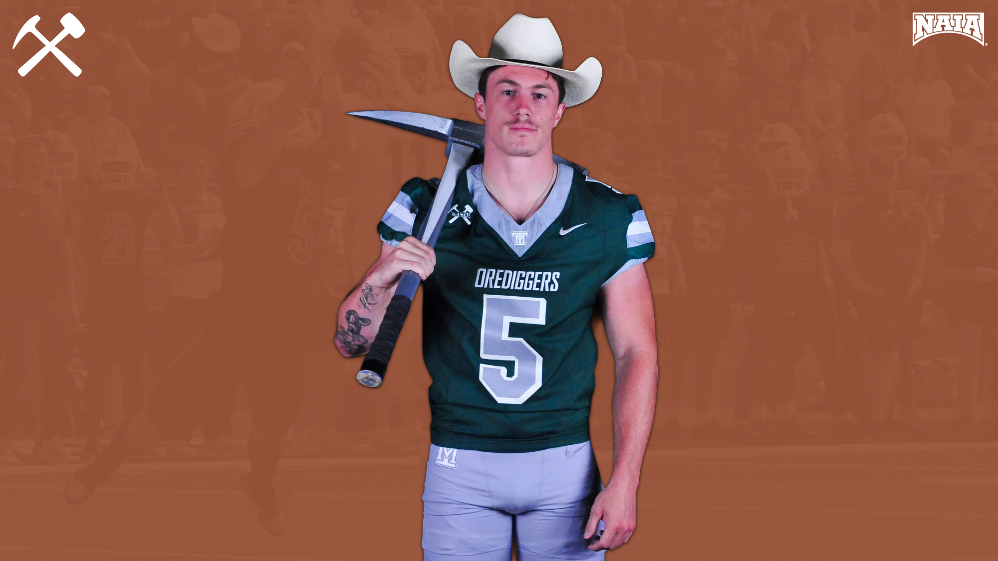 Christian Hansen stands in a Montana Tech football uniform wearing a cowboy hat and holding a pickaxe