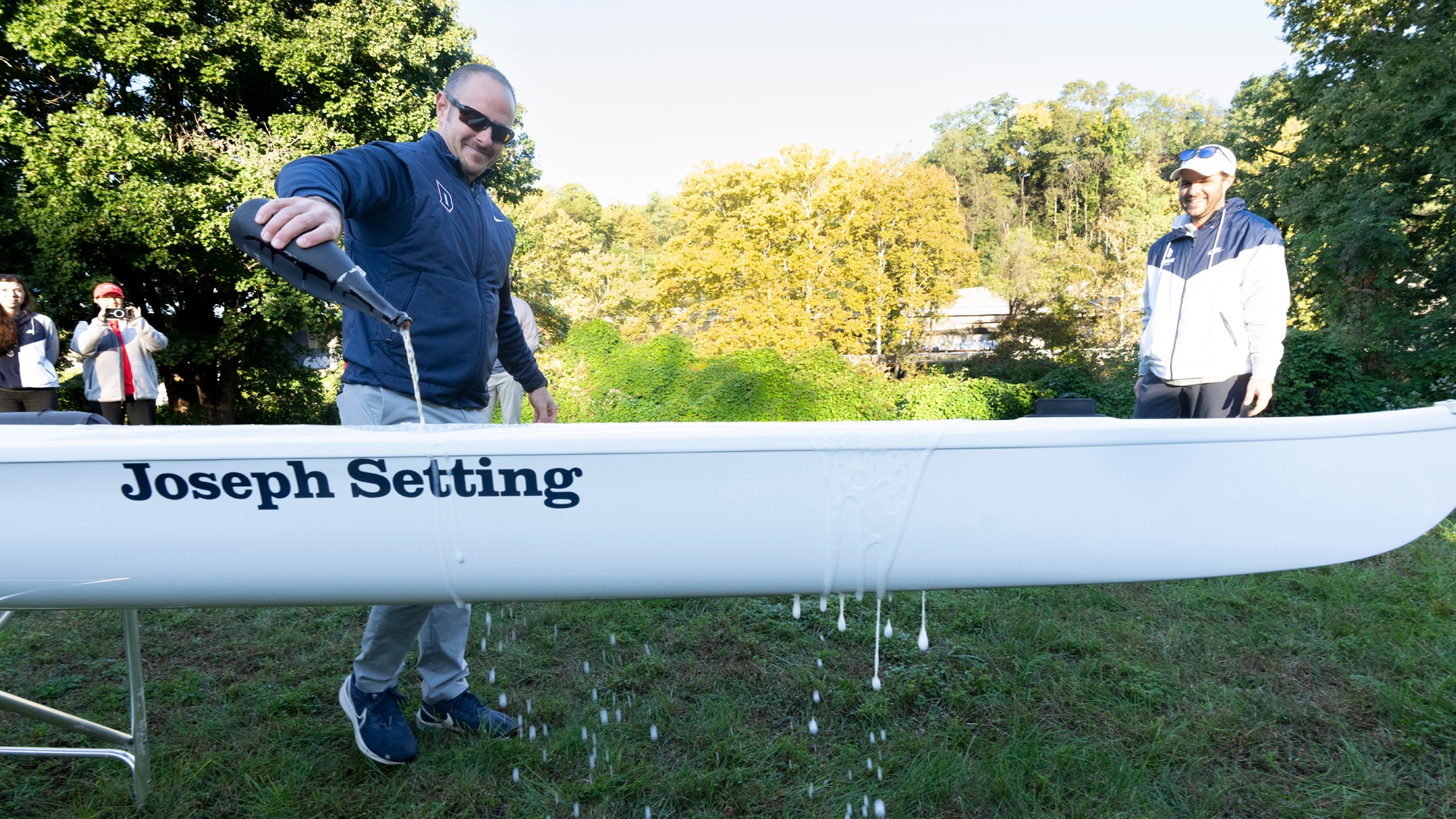 Joe Setting pours champaign over Duquesne's new GSR 8+ boat named in his honor.