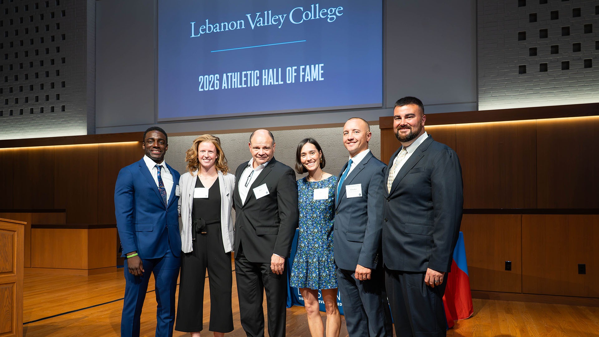 The 2026 LVC Athletics Hall of Fame inductees stand on a stage with a Lebanon Valley College Athletics Hall of Fame background screen