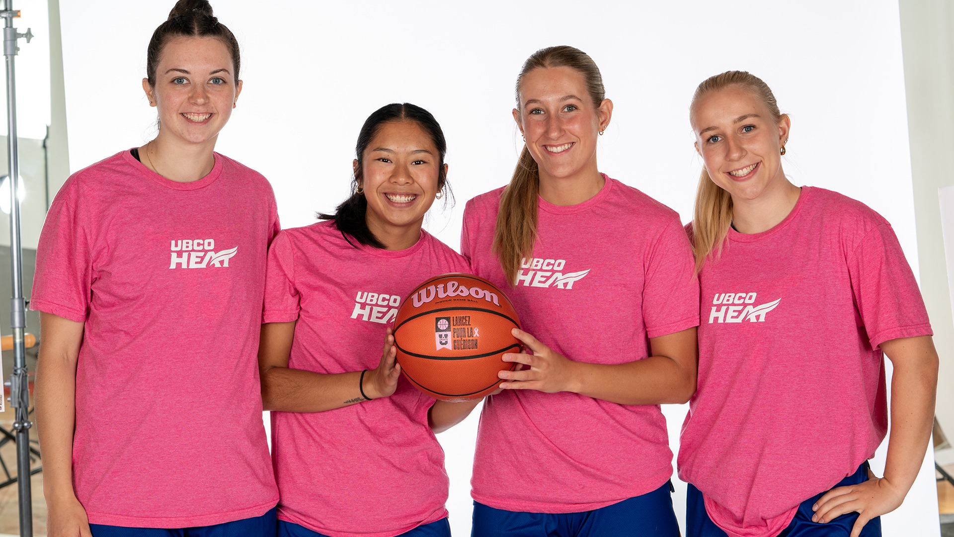 From left to right, women's basketball team members Stef Hart, Tsuki Tsuzuki, Ava Heppner and Kiana Kaczur pose in their pink-themed shirts while holding a Shoot for the Cure basketball