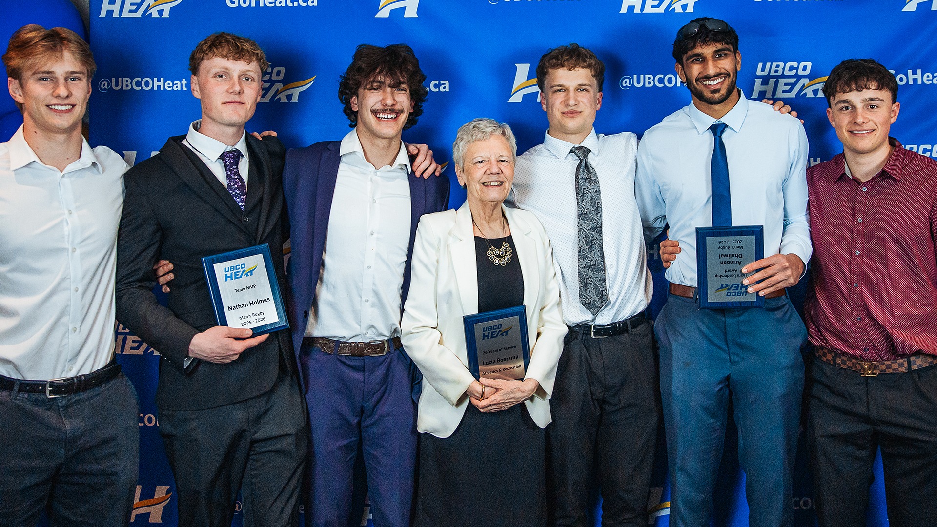 Long-time Athletics and Recreation staff member Lucia Boersma (middle) is flanked by members of the men's rugby team at the 2026 Athletic Awards Banquet at the Coast Capri Hotel.