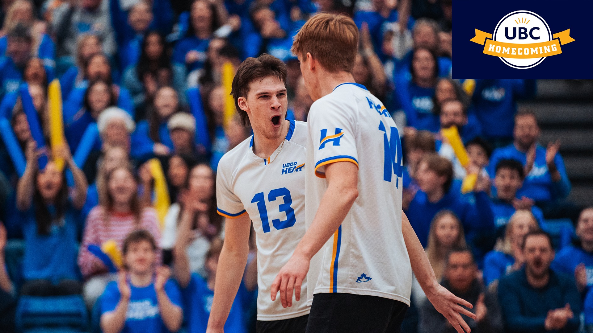 Heat men's volleyball players Thys Weststrate and Lucas Woelders celebrate a point during volleyball action at the UBCO Gymnasium. The UBC Homecoming logo is in the top right of the image.