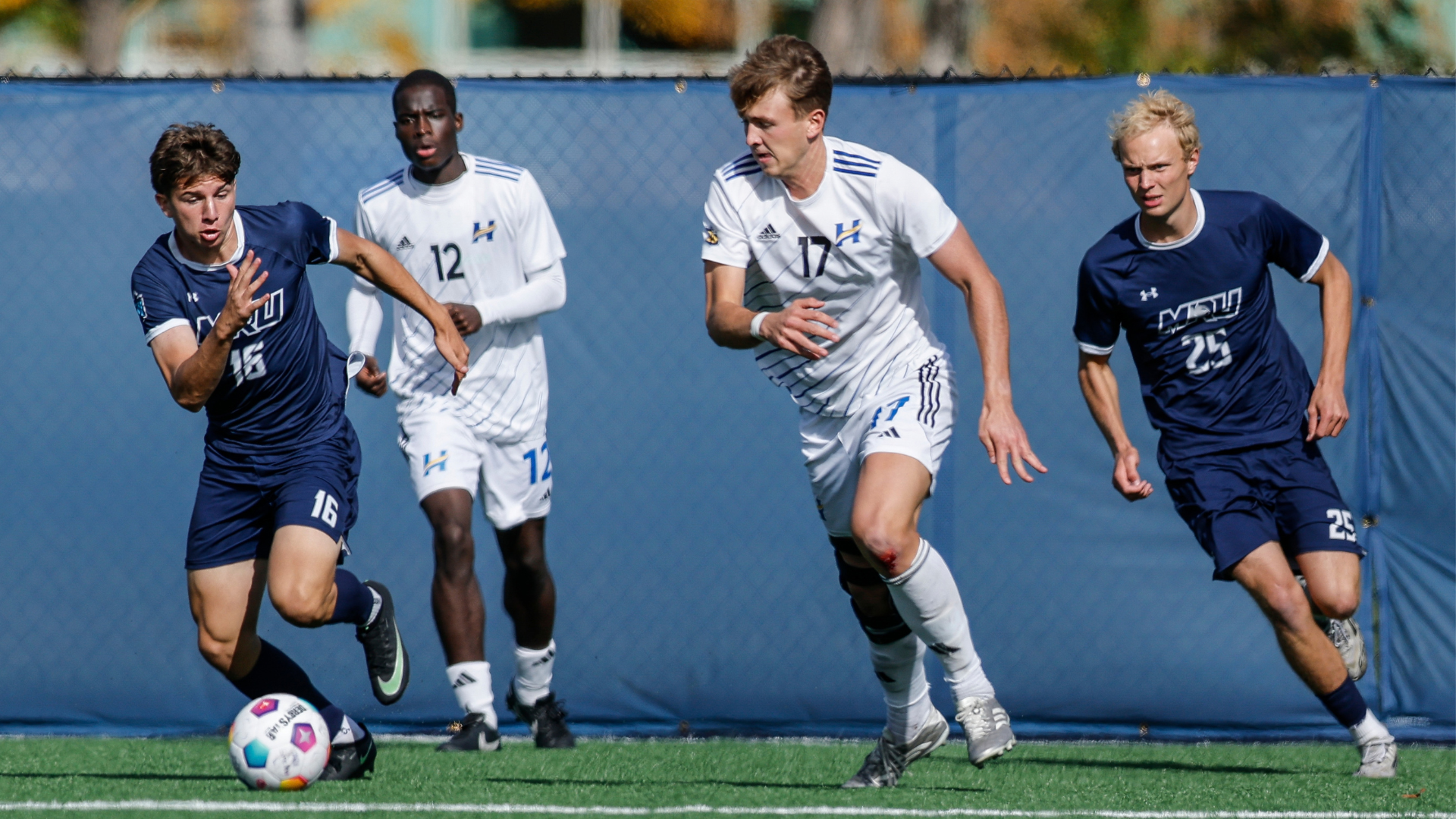Ian Klumpen of the UBCO men’s soccer team dribbles the ball against the MRU Cougars at  Mount Royal Stadium Field with Fope Amure pictured in the background