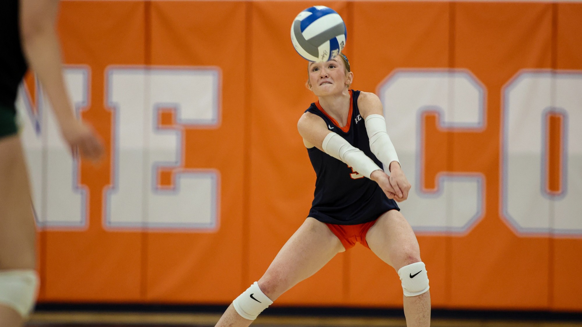 A Keystone volleyball player in navy and orange passes the ball with her forearms during a match.