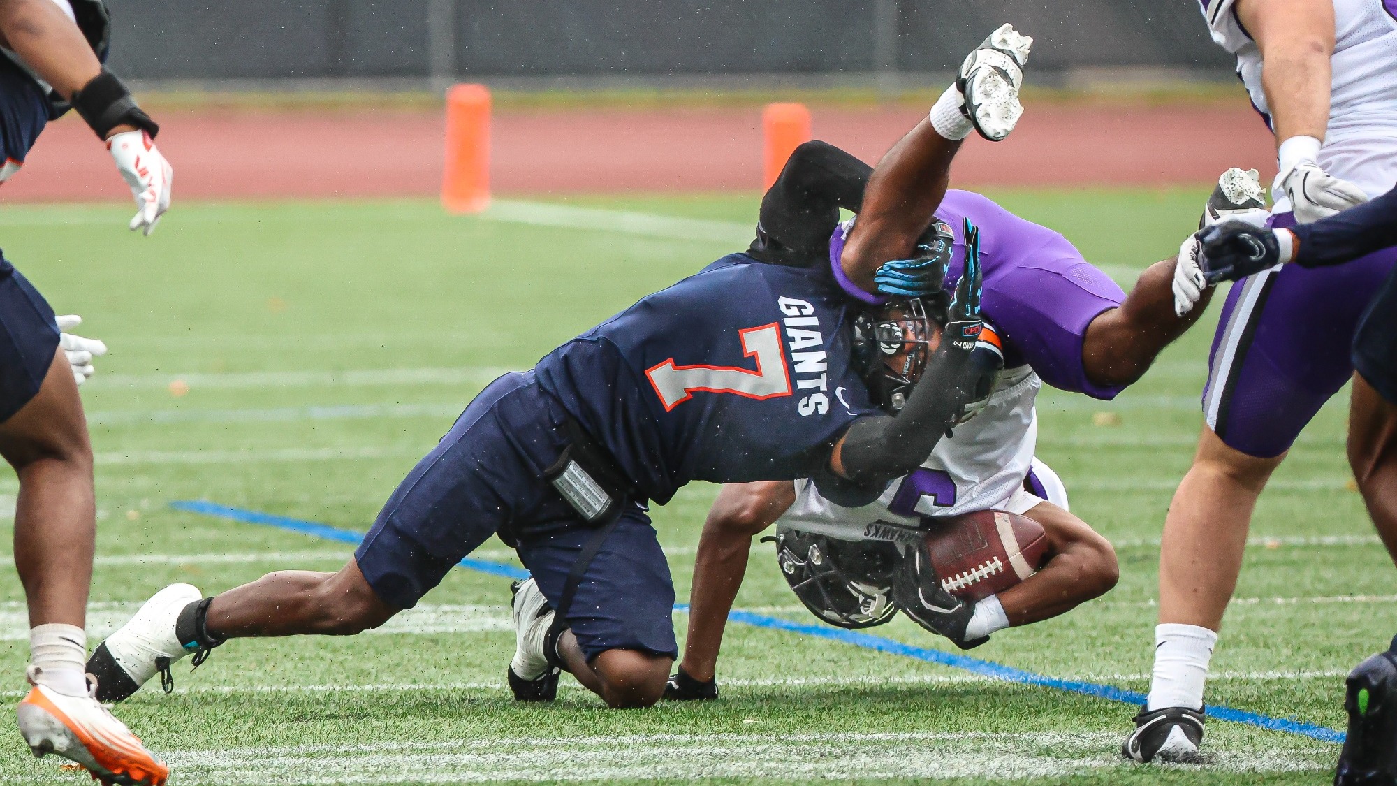 A Keystone football player wearing No. 7 tackles a ball carrier in white and purple near the end zone.
