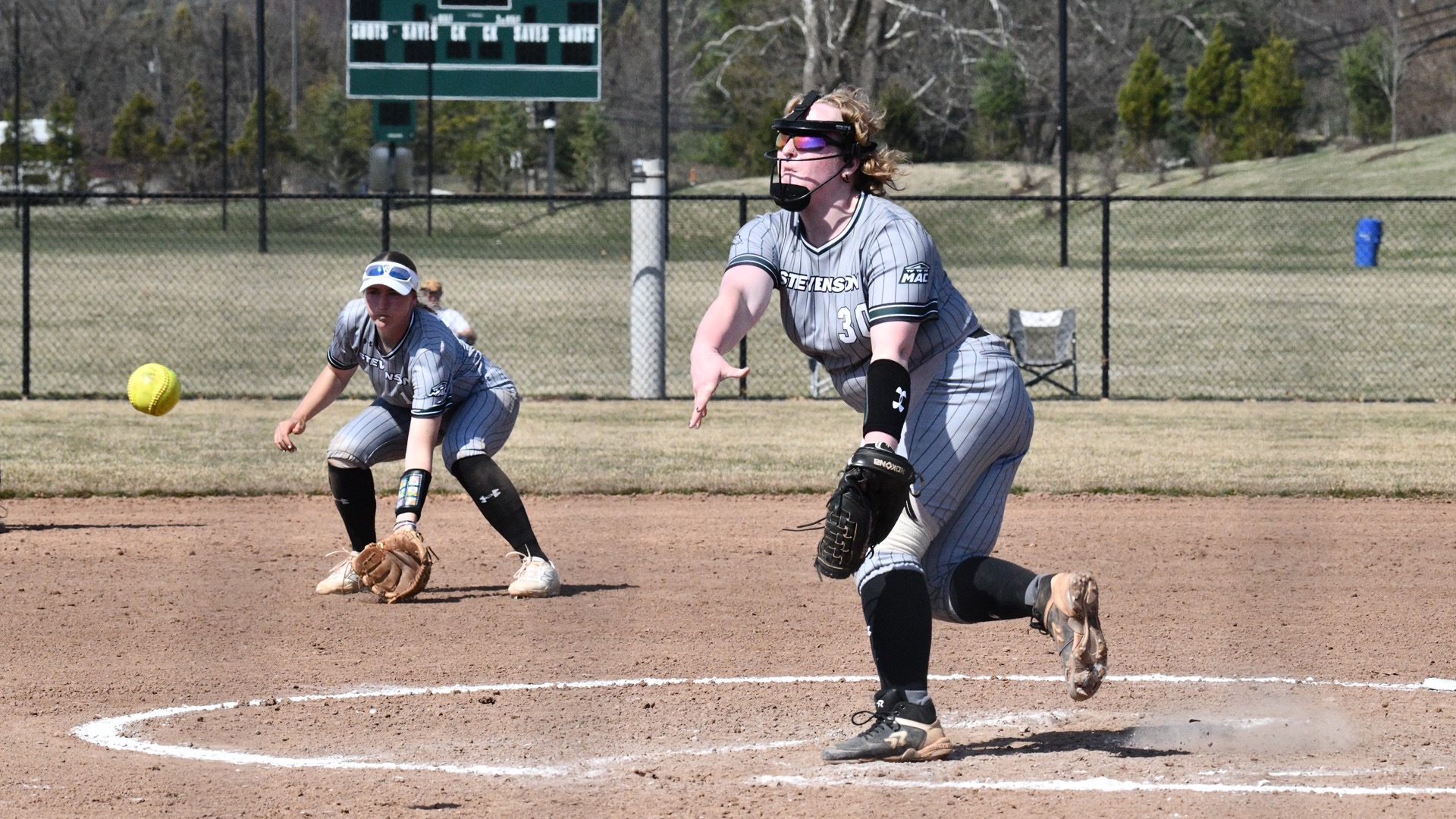Ky Vaughn throwing out a pitch, with Tessa Boswell in the background ready to field the possible hit into play