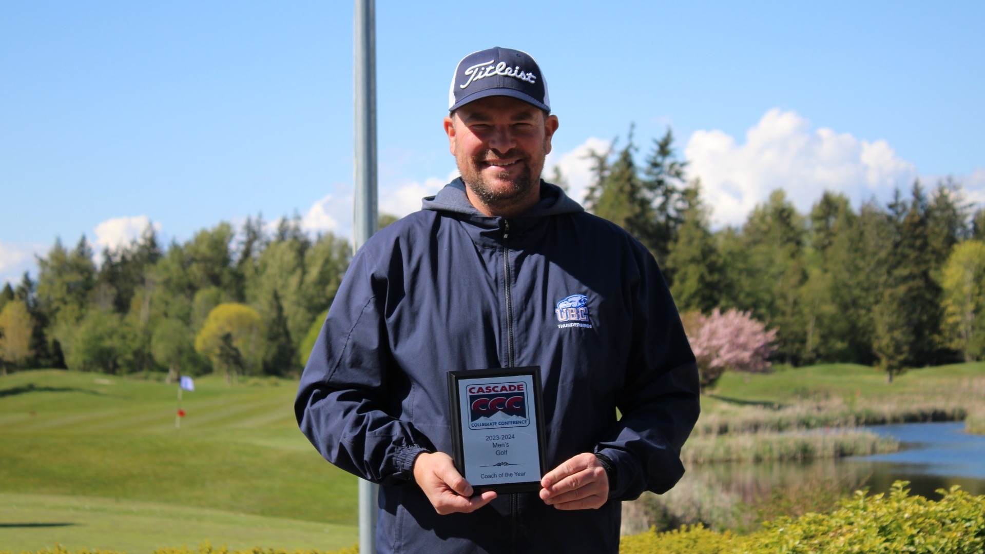 Chris MacDonald smiling and posing with a plaque after winning Cascade Collegiate Conference Men's Coach of the Year