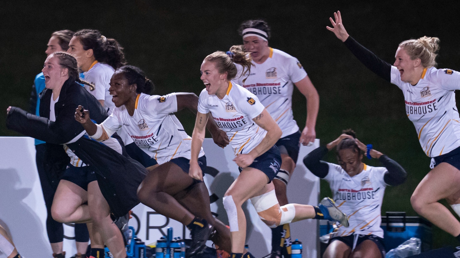 UBC Thunderbirds women's rugby players streaming toward the middle of the pitch from their sideline, all smiling and yelling in celebration of their win over Laval in the U SPORTS Championships quarter-final
