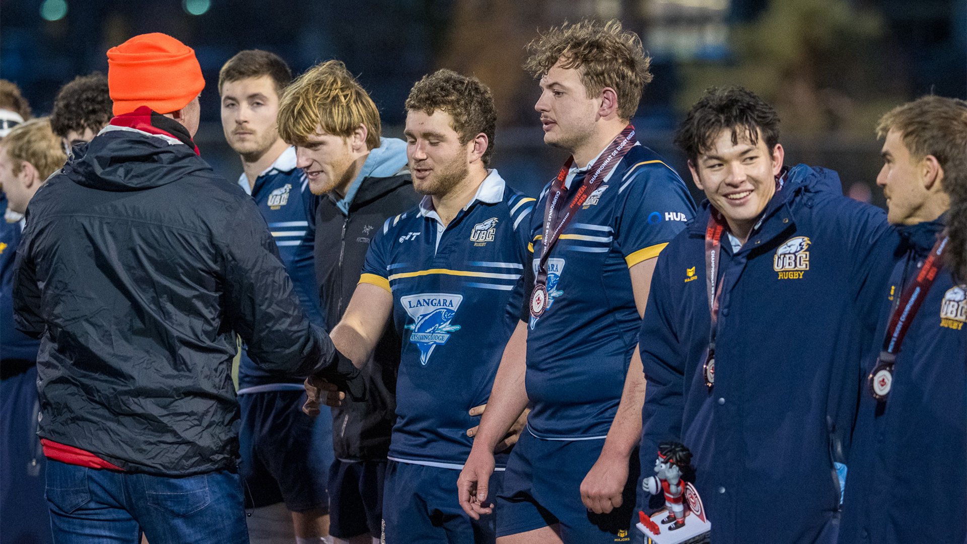 UBC Men's Rugby players smiling and standing in line to receive their bronze medals after defeating the Victoria Vikes at the 2025 Canadian University Men's Rugby Championship