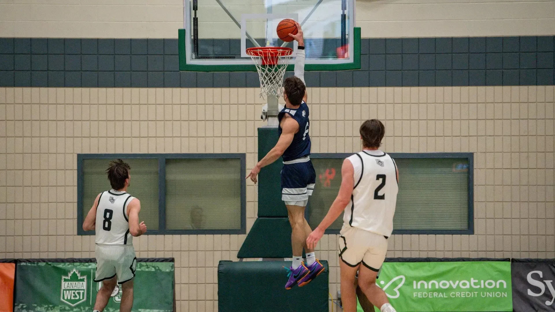 UBC Thunderbirds men's basketball player Nikola Guzina throwing down a one-handed dunk, seen from behind from the opposite baseline