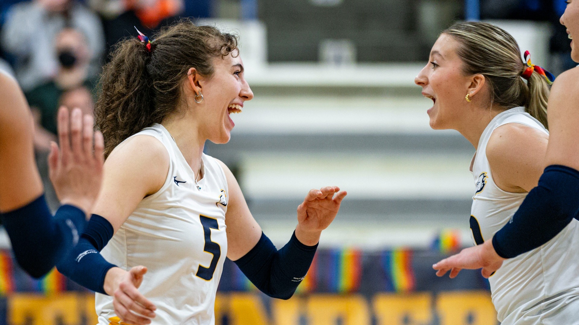 UBC Thunderbirds women's volleyball players Issy Robertshaw and Ella Ungemach yelling toward one another in celebration, both looking delighted after the T-Birds scored a point