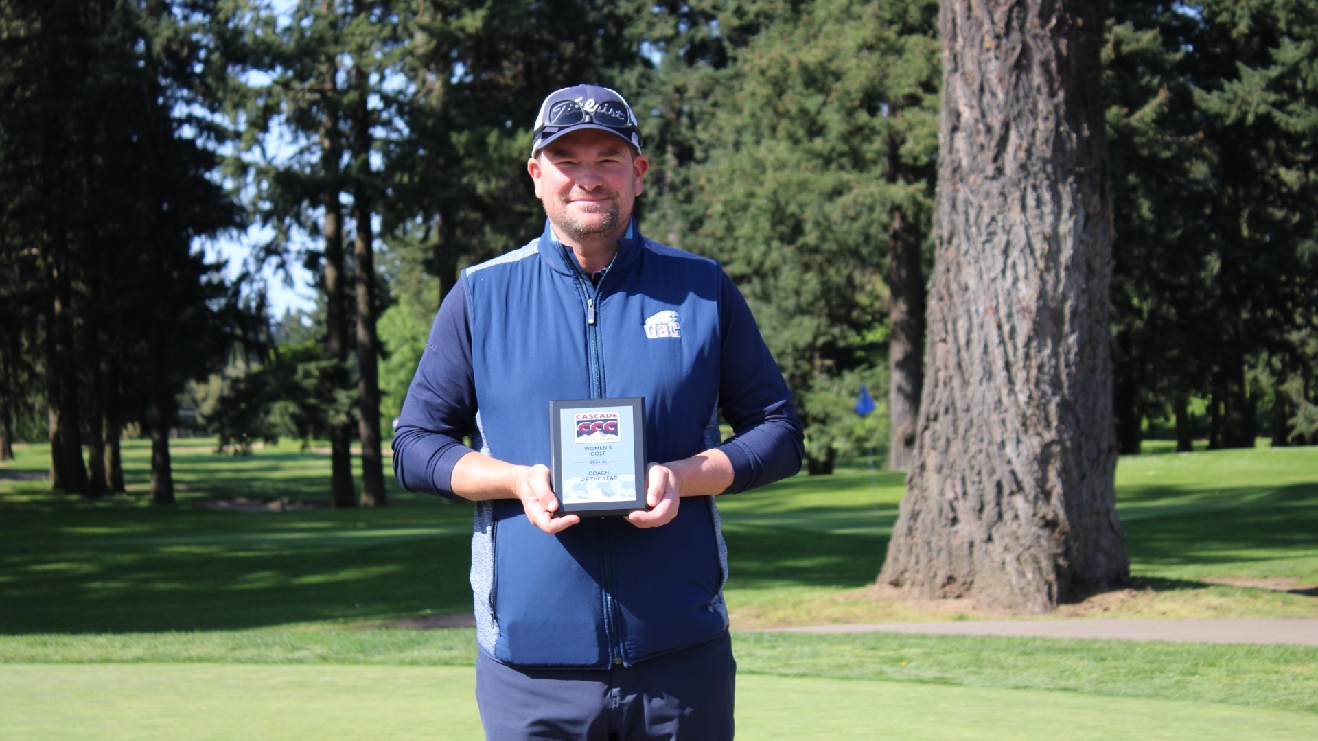 Chris MacDonald smiling and posing with his plaque after being named 2025 Cascade Collegiate Conference Women's Golf Coach of the Year