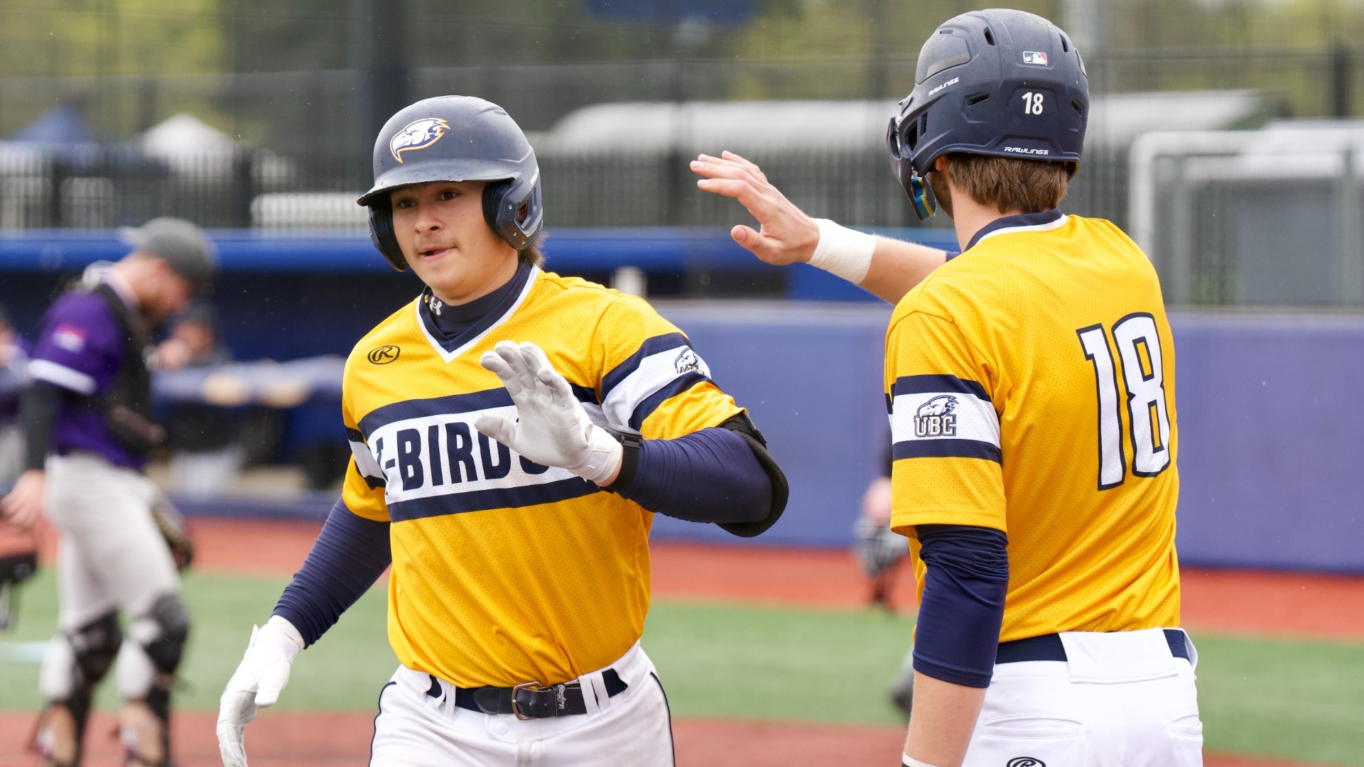 Two UBC players are about to high five as one jogs towards the dugout