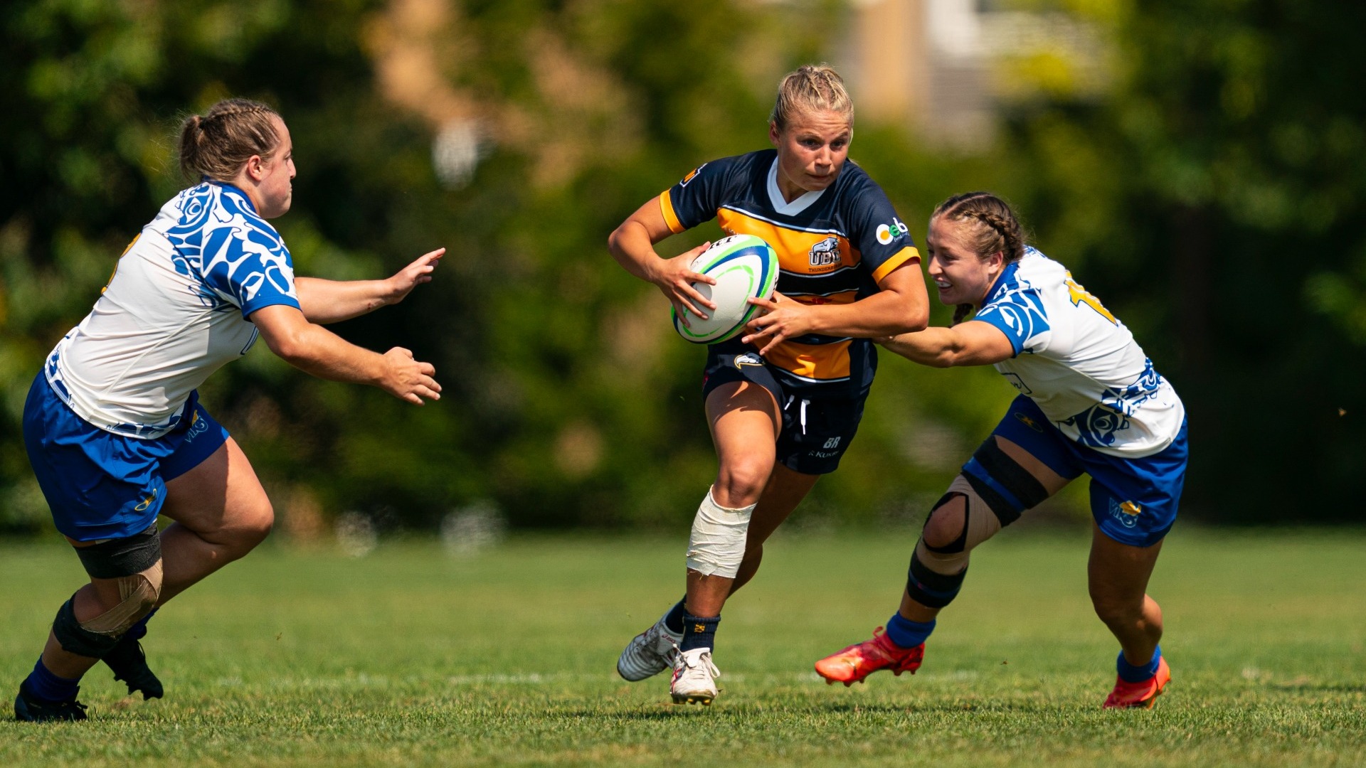 Brooke Roddham turning up the pitch with the ball, Victoria Vikes players on either side of her reach toward her