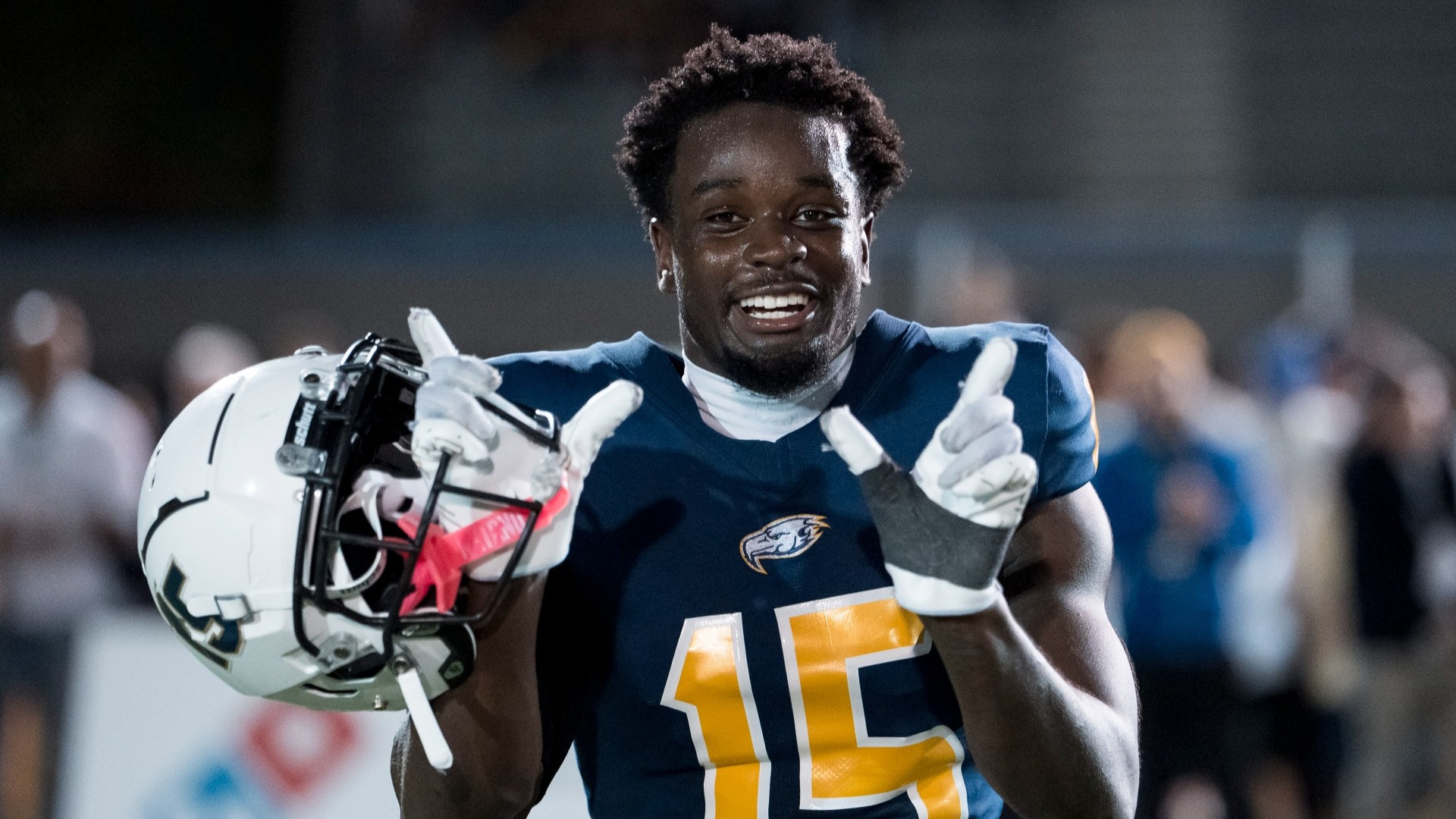 Ben Sangmuah with his helmet off, grinning directly into the camera in semi closeup, making a W sign with his two hands to celebrate the UBC Thunderbirds win over the Calgary Dinos