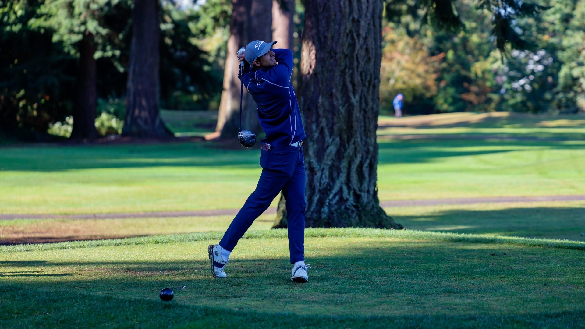 Aneesh Kaura holding his follow through and watching his shot after hitting a driver from a shaded tee box