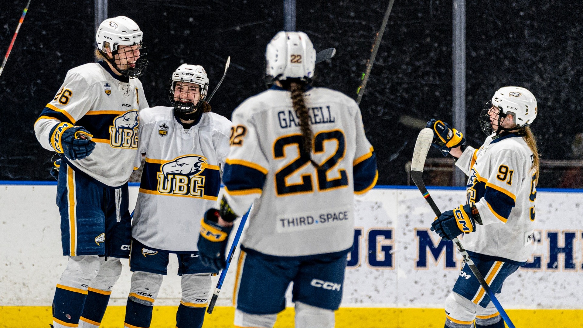 UBC Thunderbirds women's hockey players Jacquelyn Fleming, Grace Elliot, Sophia Gaskell and a fourth player all celebrate a goal on the ice, Elliott grinning widely