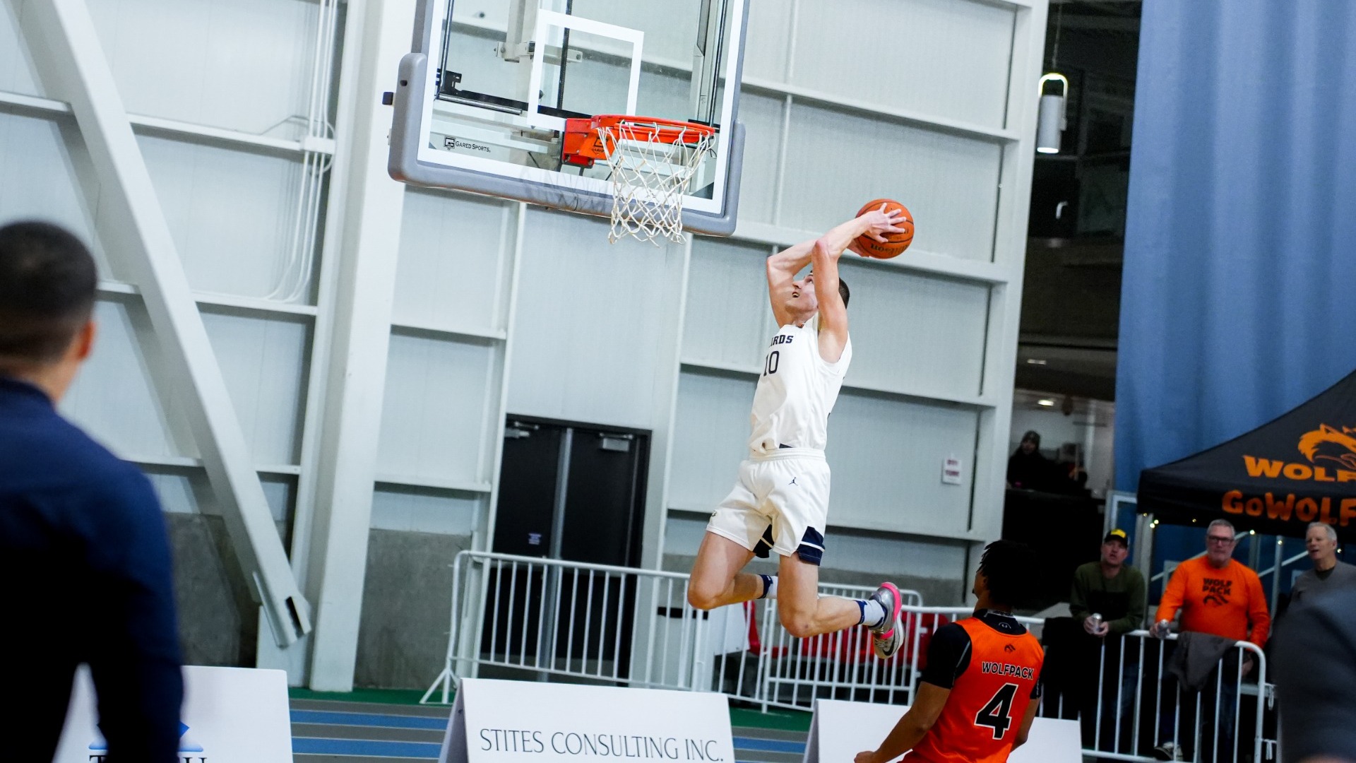 UBC Thunderbirds men's basketball player Gus Goerzen rising in the air, the ball in his hands and pulled back behind his head, clearly about to throw down a big, in-game dunk against the Thompson Rivers WolfPack