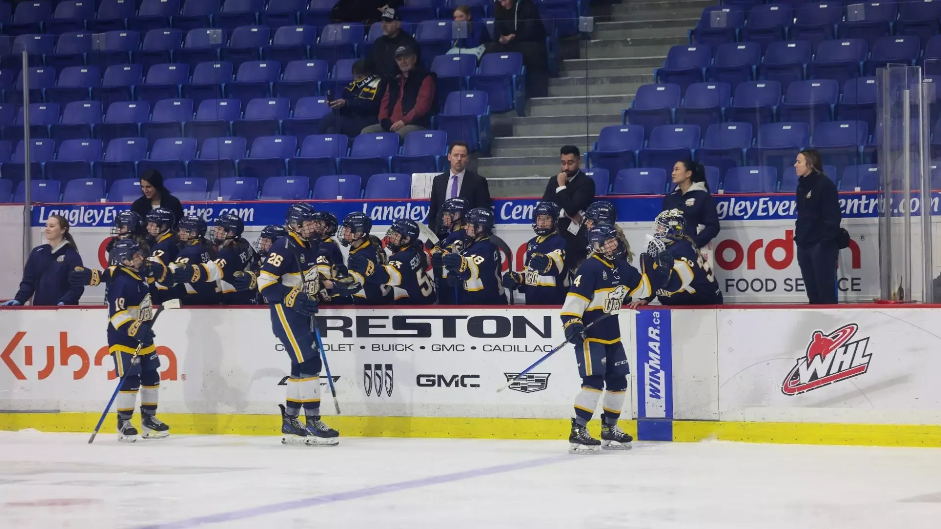 UBC Thunderbirds women's hockey celebrating a goal with three players skating by their bench for fist bumps