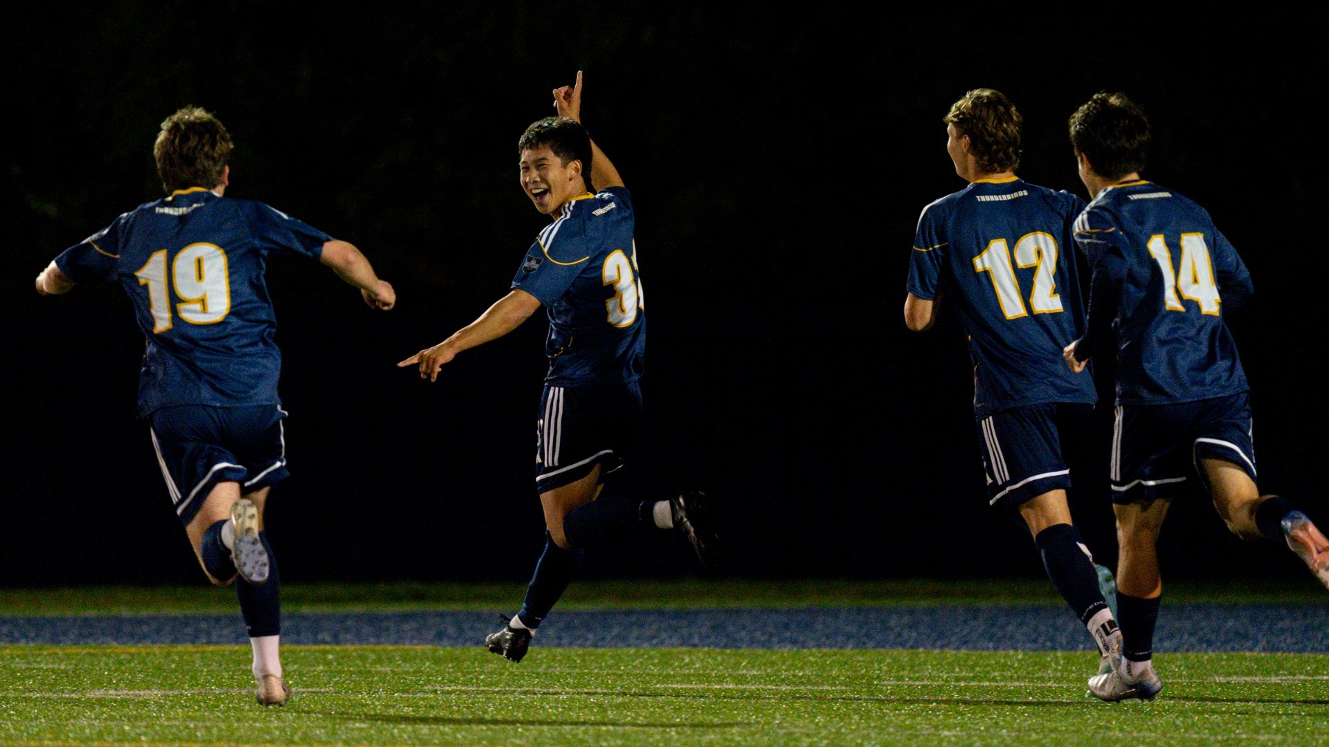 UBC Thunderbirds men's soccer player grins widely, pointing his finger in the air as he runs away from his teammates after scoring his first goal of the season in his final regular season game with UBC