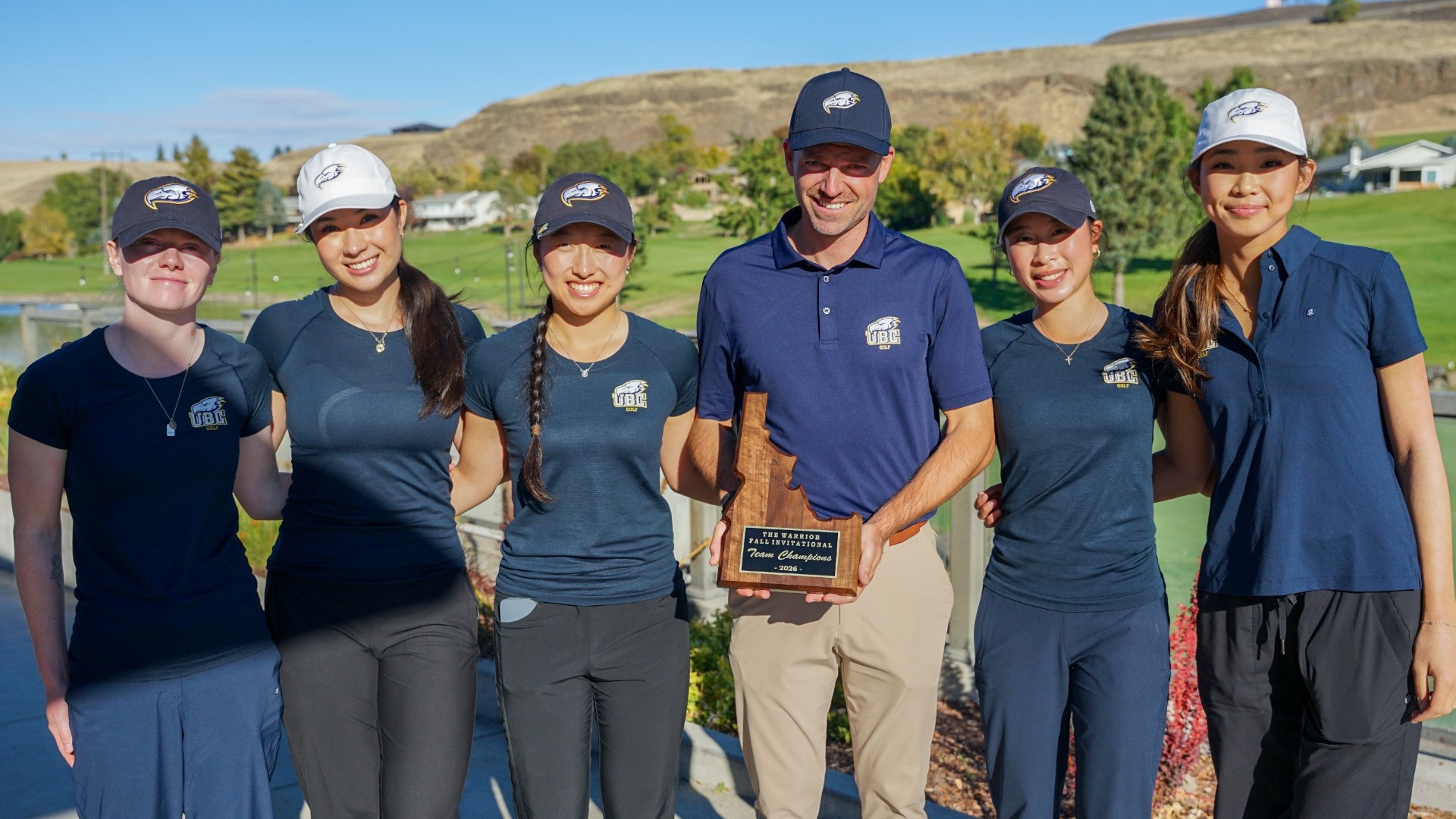 The UBC Thunderbirds women's golf team smile and pose with coach Cory Renfrew, while holding a trophy after winning the 2026 Lewis-Clark State Fall Invitational