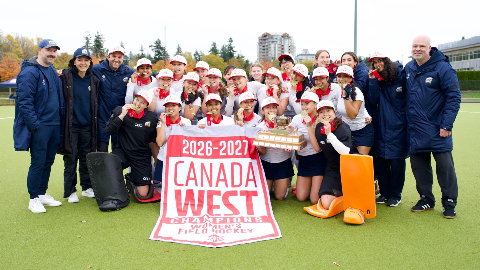 The UBC T-Birds bite their gold medals while posing with the CW banner after a game against the UVic Vikes on Oct. 25, 2026