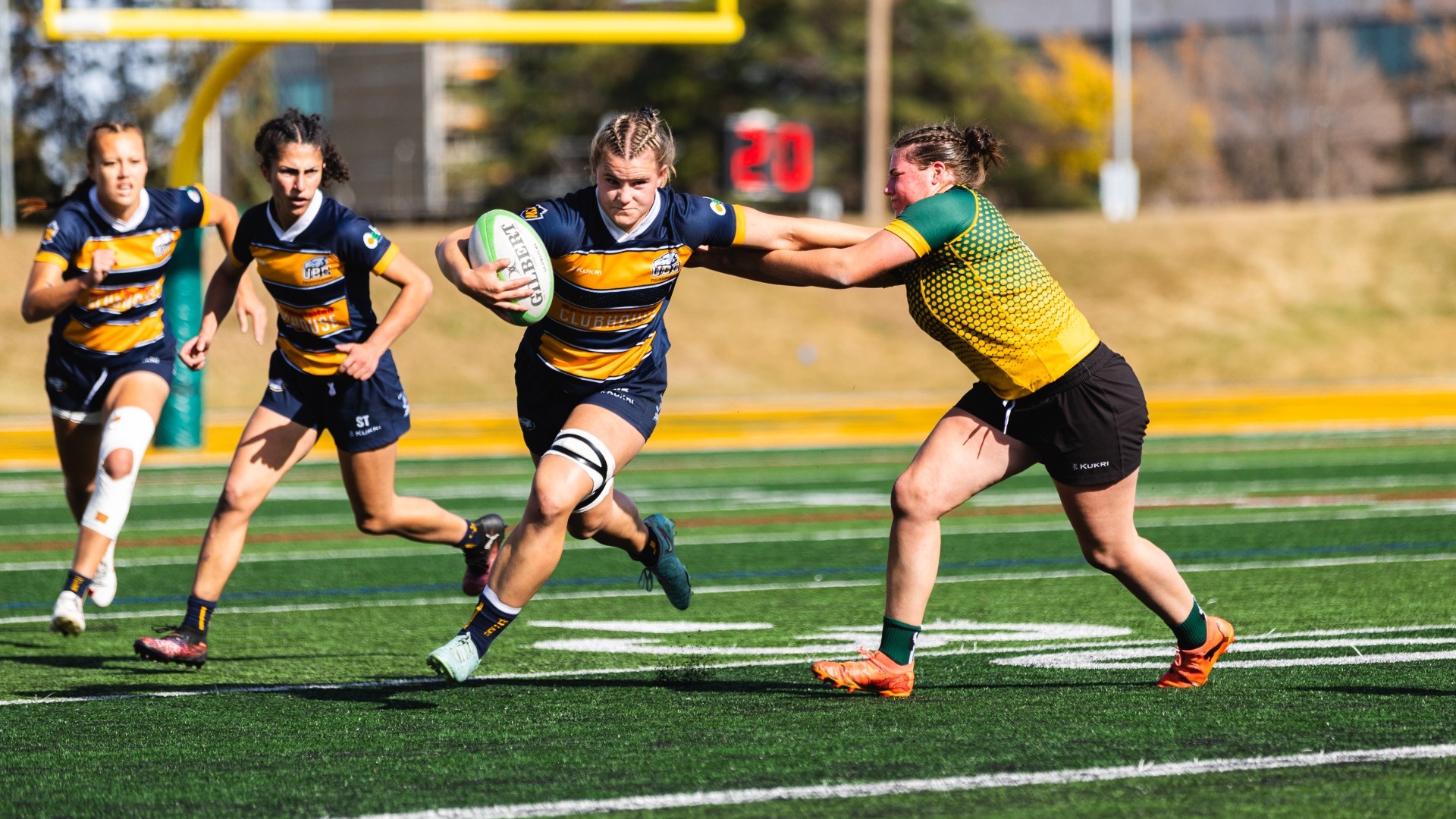 A UBC player stiff-arms an Alberta defender while running down the field with the ball