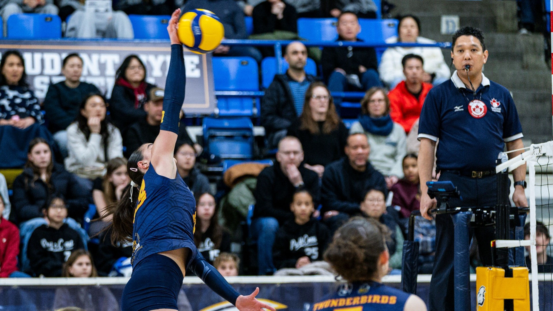 A UBC player is mid-air and about to hit the ball over the night along the sideline