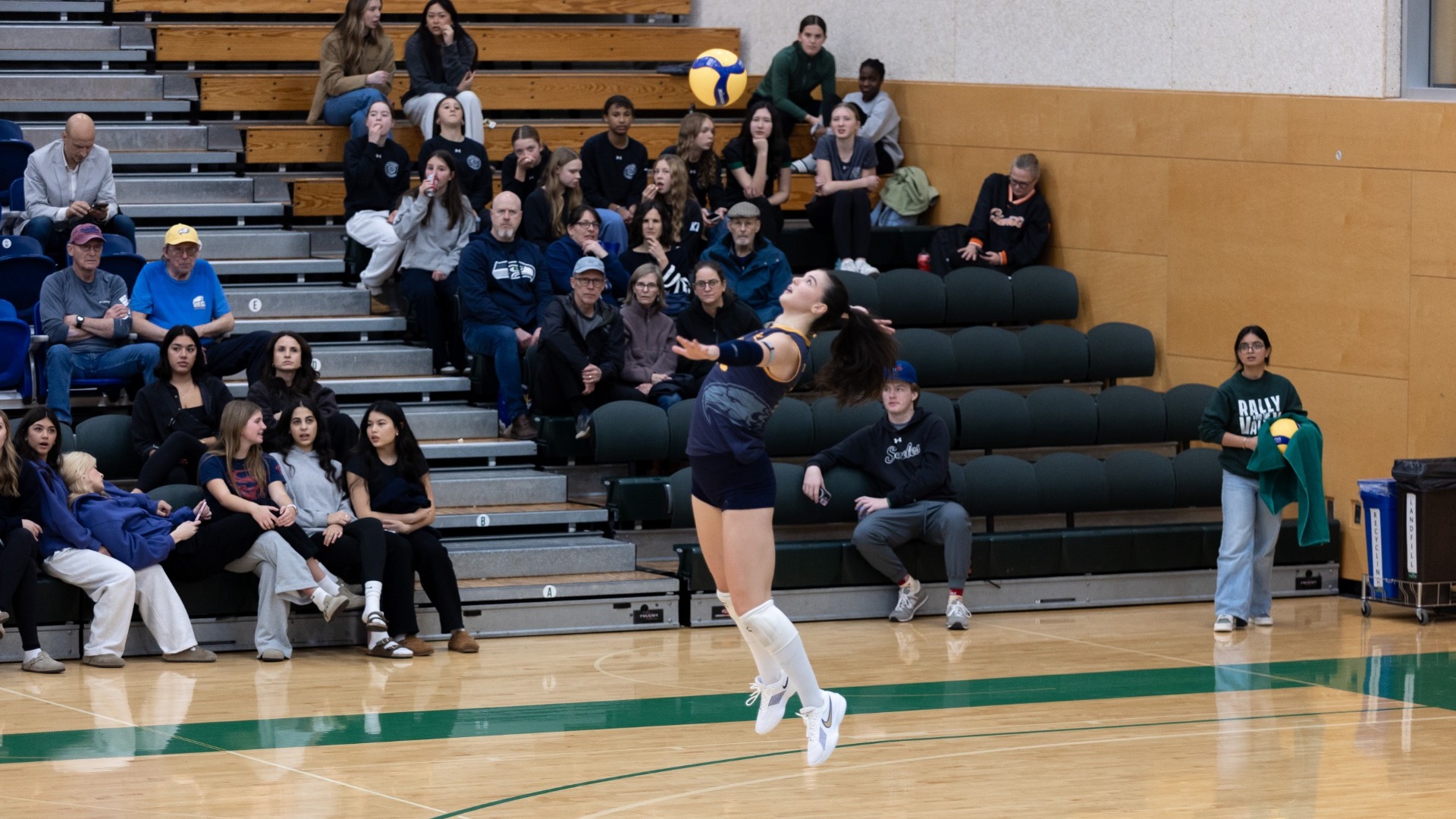 A UBC player is mid-air, about to hit a serve