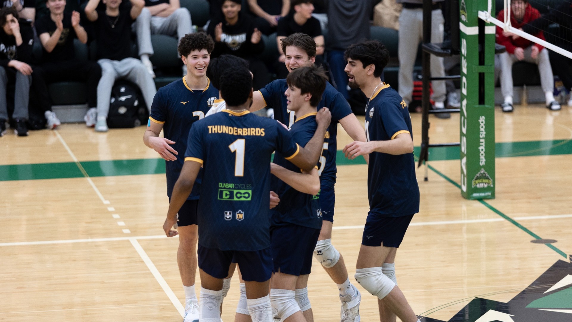 All six UBC Thunderbirds men's volleyball player on the court come together, grinning, to celebrate a point