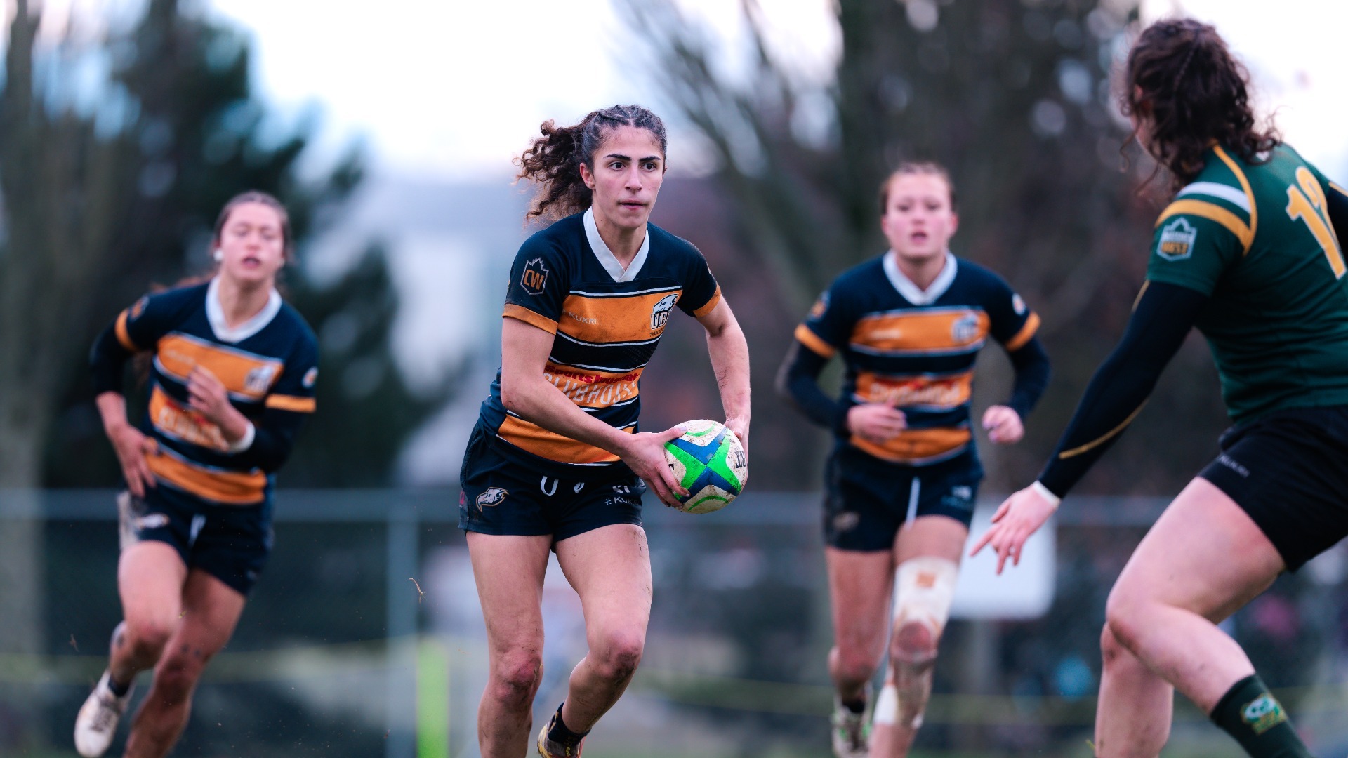 A UBC player runs towards a defender with the ball, with a couple teammates behind her