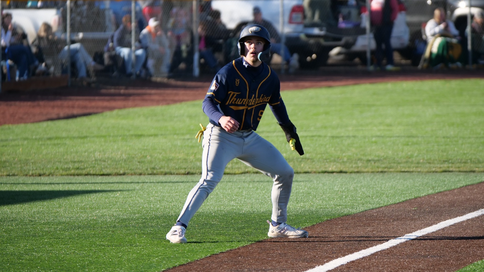 UBC baseball runner on third base, standing in foul territory and looking up intently, presumably at a ball in the air