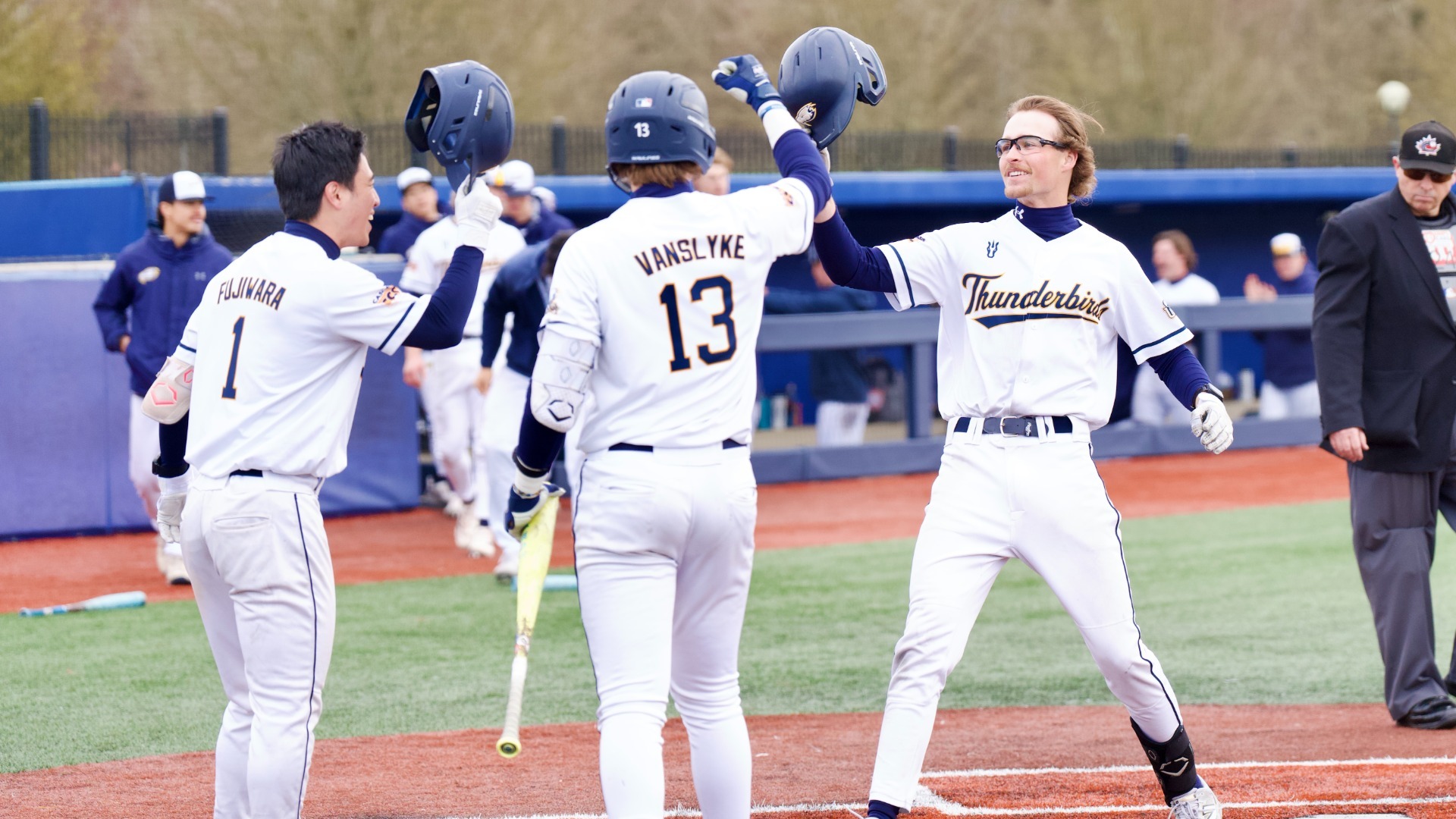 UBC baseball players Lou Fujiwara, Matt Vanslyke, and Calvin Warrillow all smiling and tapping helmets to celebrate Warillow's homerun