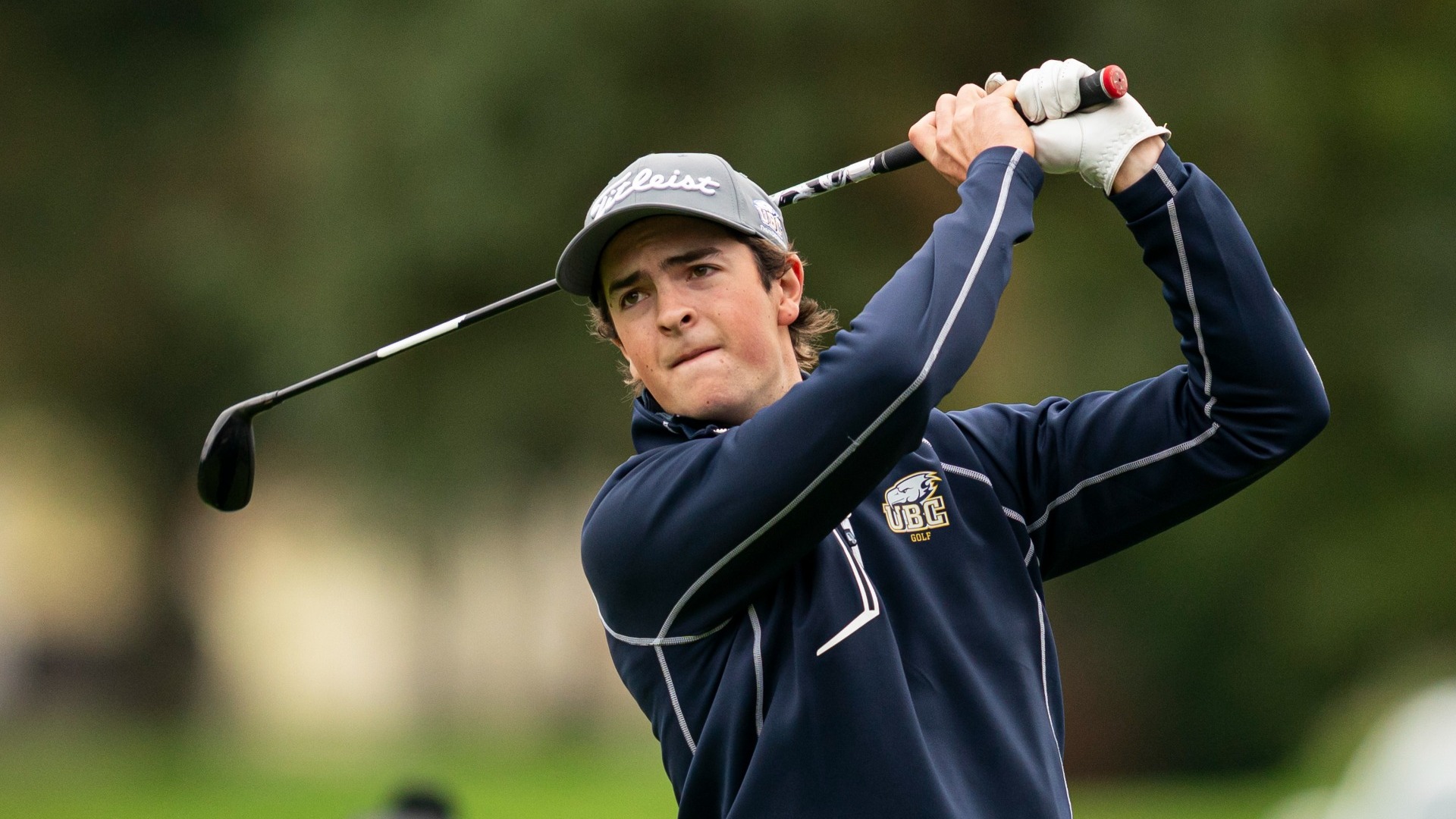 UBC Thunderbirds golfer Leighton Wright seen in semi-closeup, holding his driver behind his head in a follow through while watching his ball