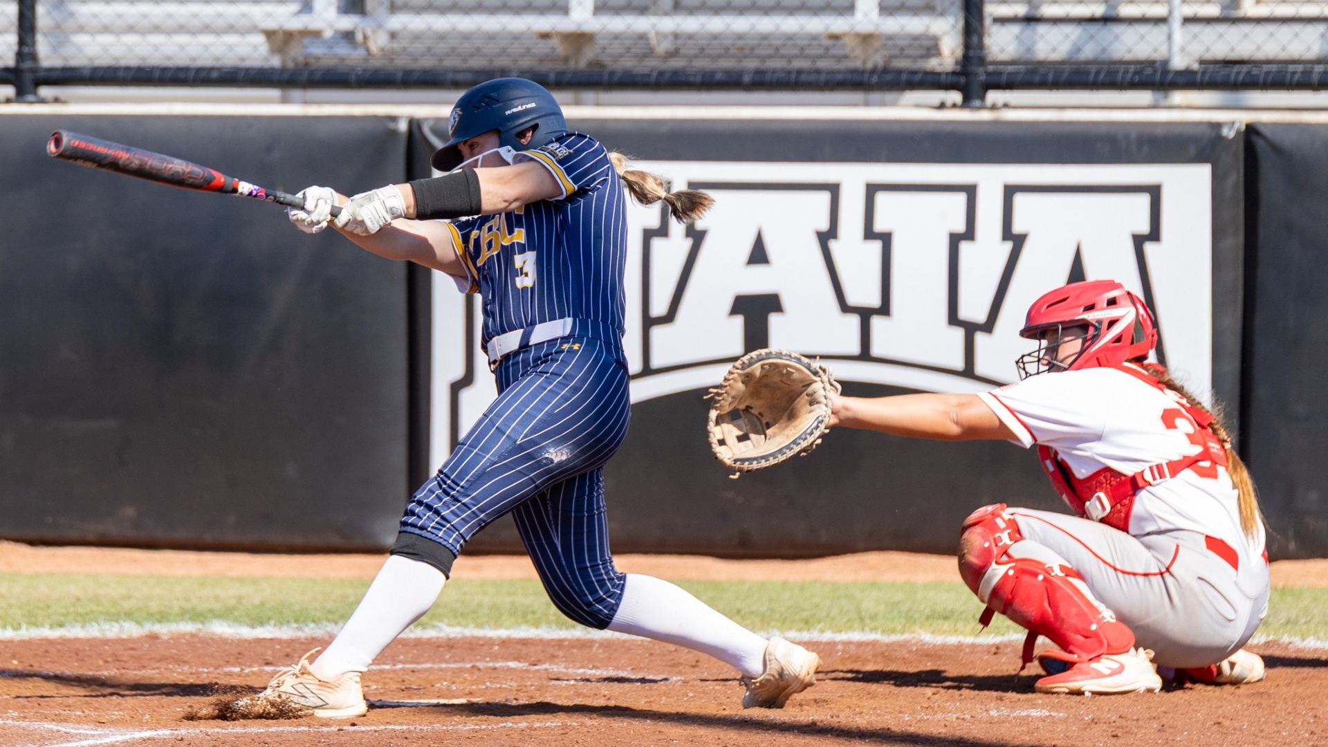 Tegan Harnett is mid-swing on a hit with the catcher reaching out behind her 