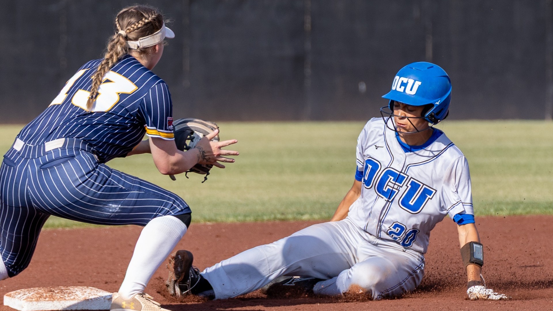 A UBC player waits at second base to try and tag out a sliding OCU baserunner