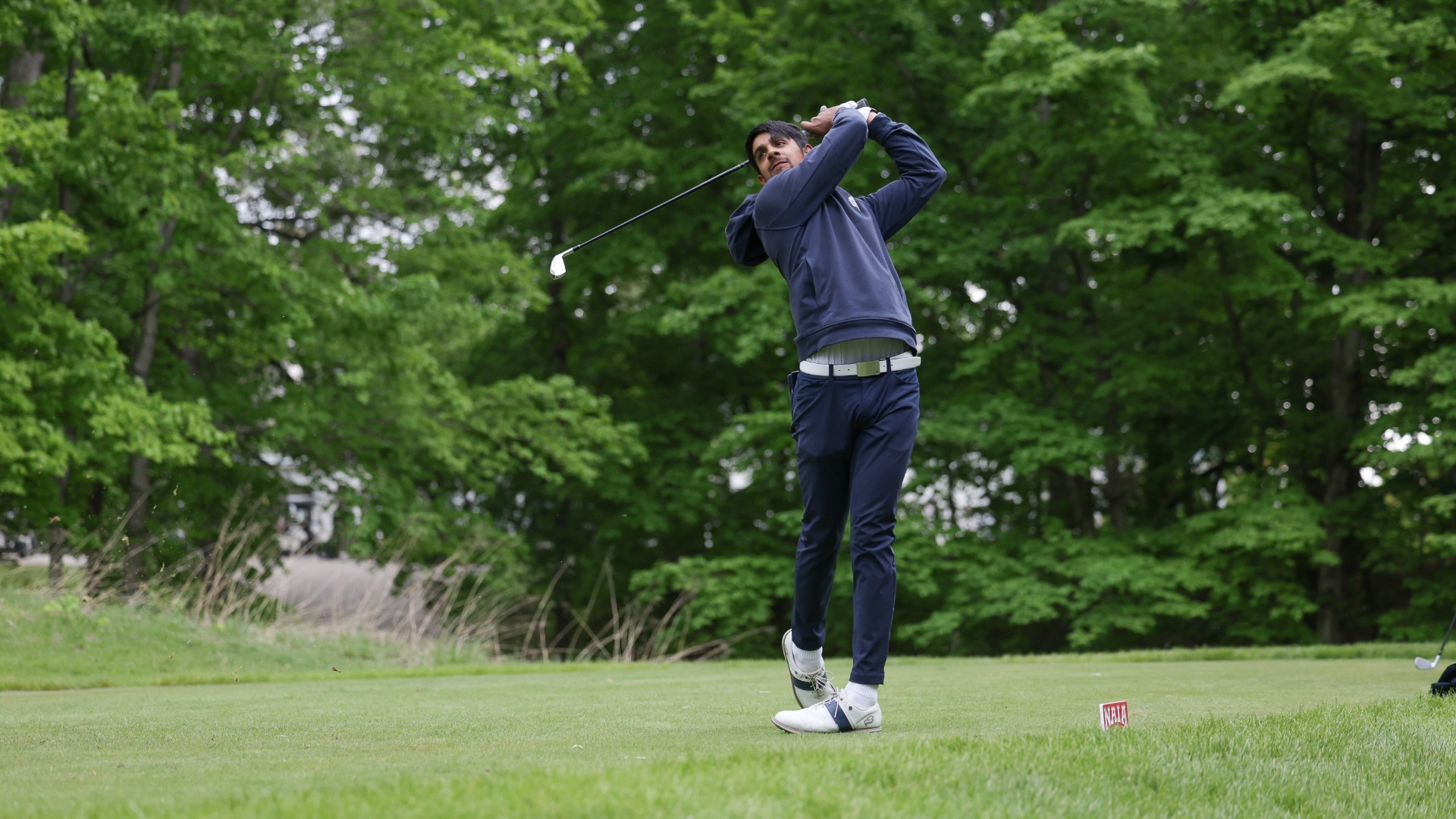 UBC Thunderbirds golfer Aneesh Kaura seen from a low angle, twisted in his follow through, driver wrapped around him, as he watches his tee shot