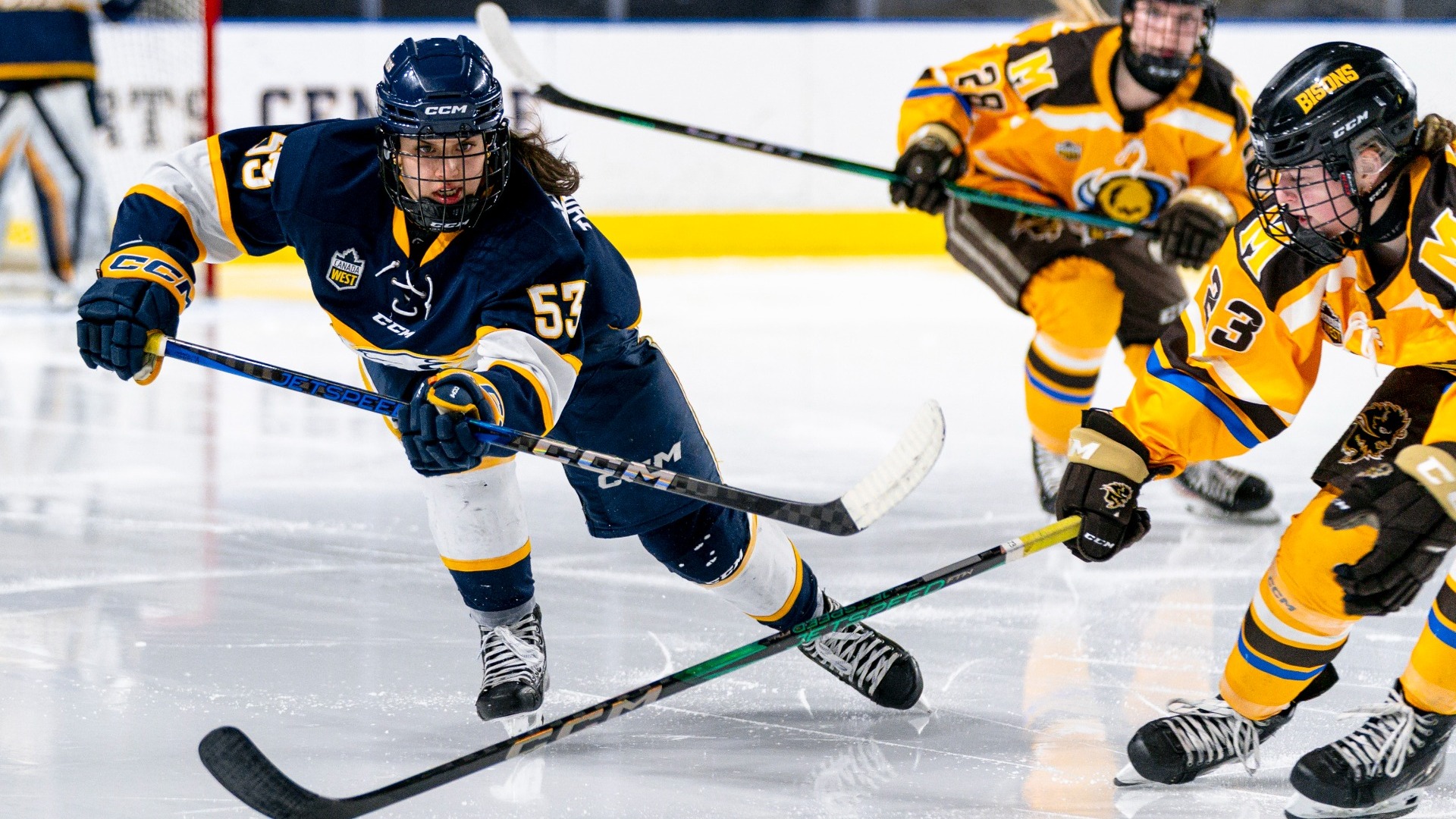 UBC Thunderbirds forward Vanessa Schaefer looking intently up ice after passing the puck forward, a Manitoba Bisons player is in the process of stick-checking her