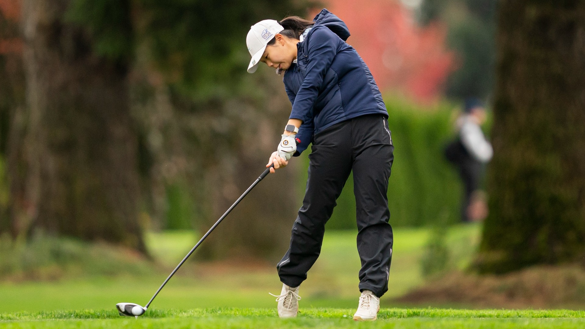 UBC Thunderbirds first-year Grace Yao hitting driver off of the tee, the ball just beginning to fly off the club, her sweatshirt billowing with the momentum of her swing