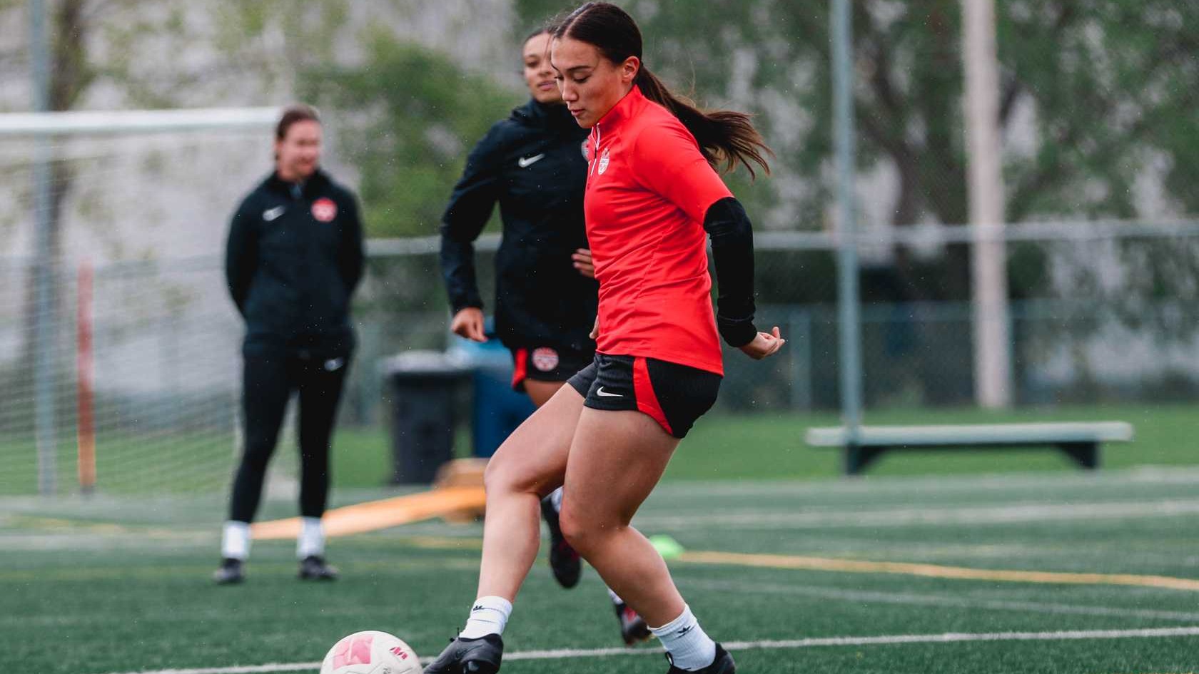 Sienna Gibson kicks the ball during a practice drill while wearing a Team Canada jacket