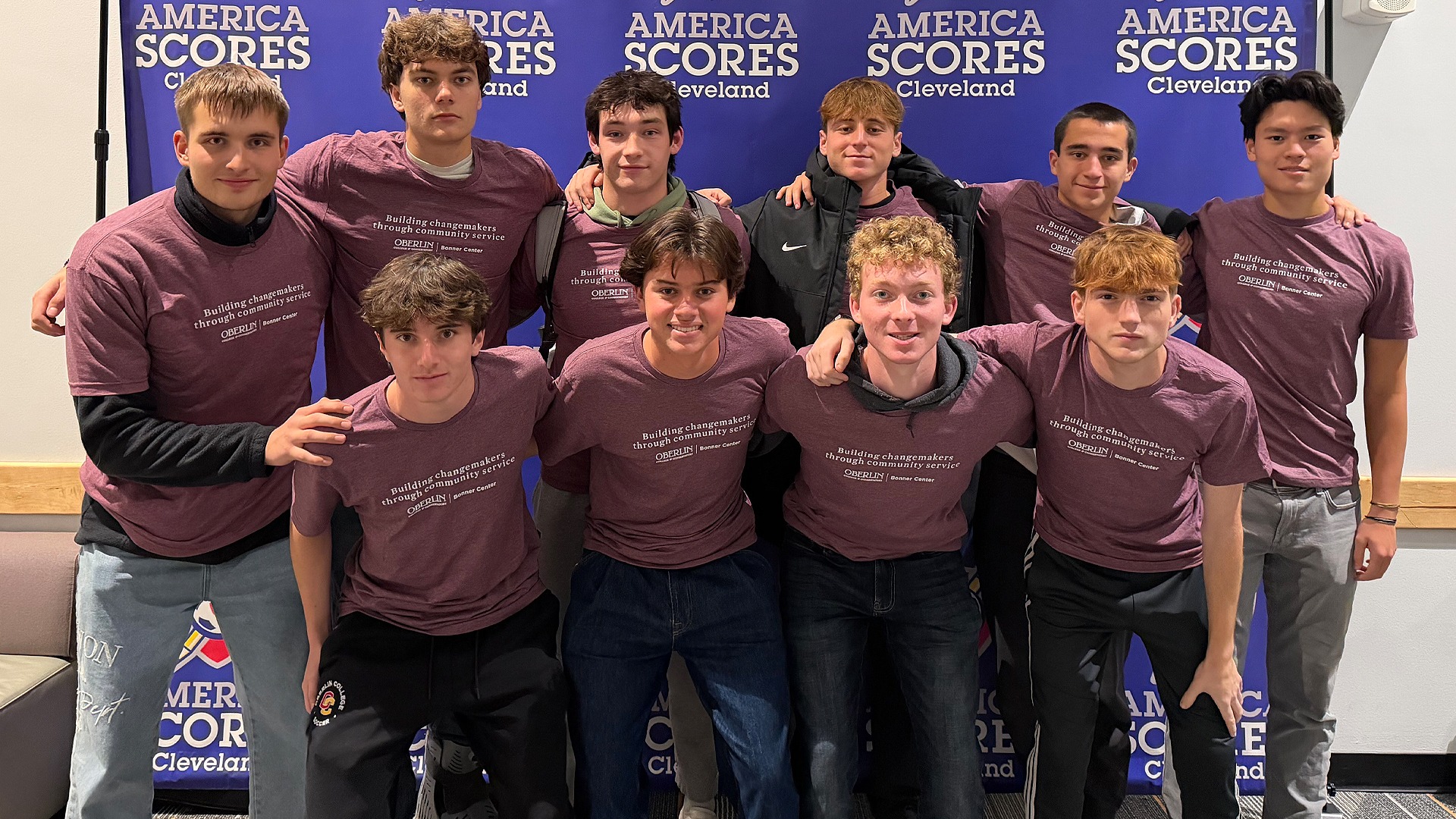 Men's Soccer team smiling in front of an America SCORES backdrop