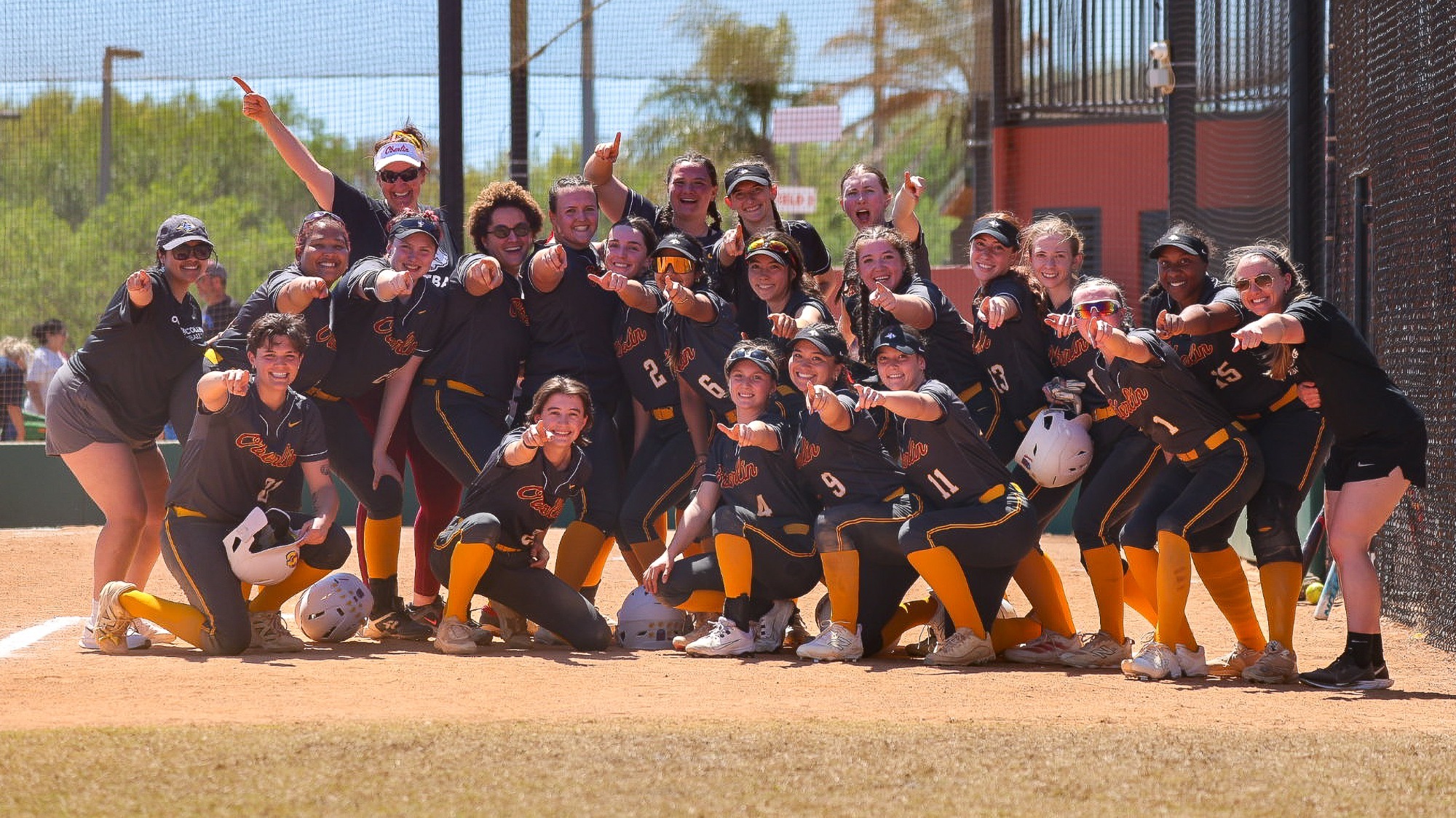 OBerlin College Softball team and coaches smiling for a team photo and pointing at camera