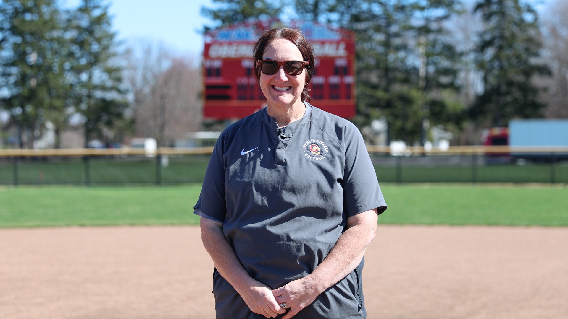 Julie Pratt smiling at camera during interview in front of softball scoreboard