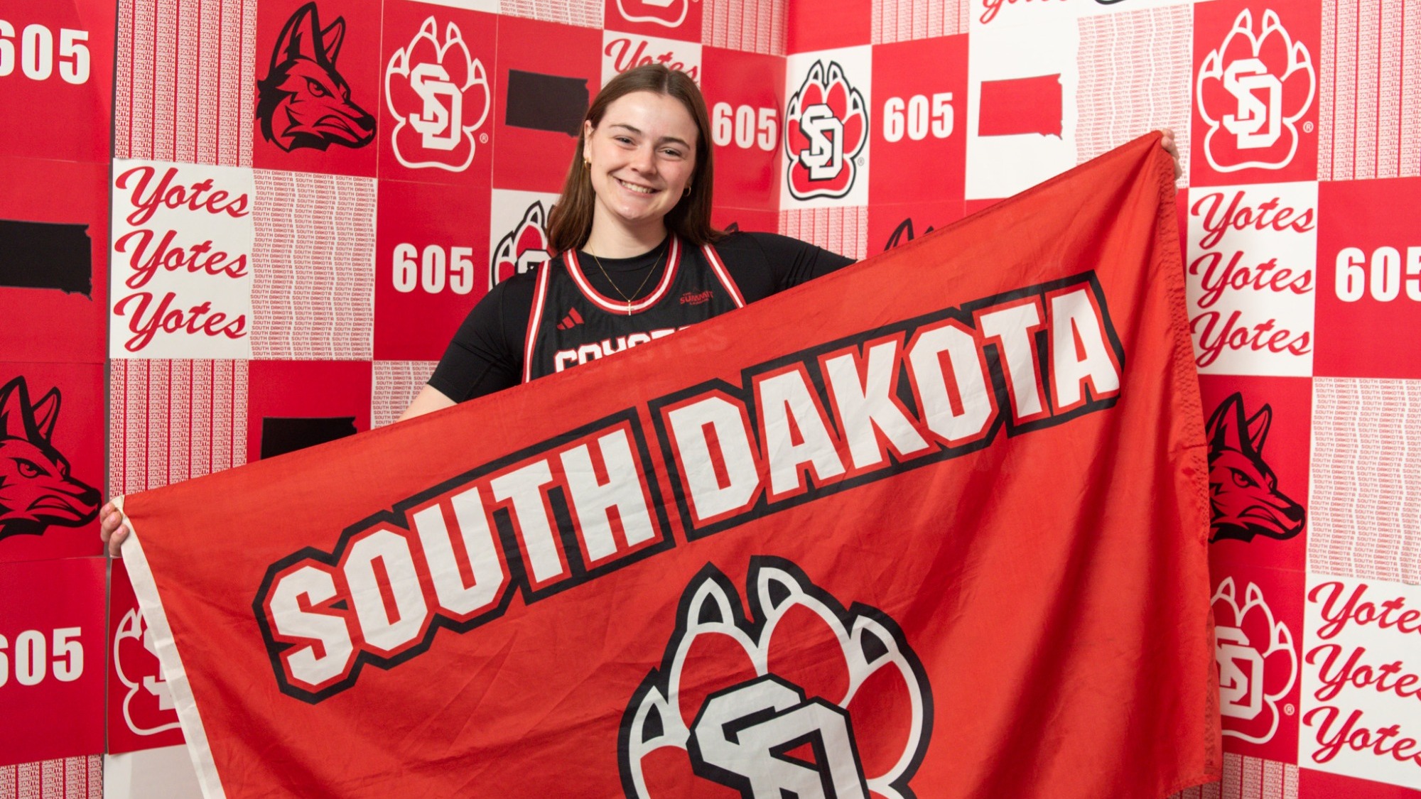 Ava Miller poses for a photo in a USD jersey and is holding a South Dakota flag