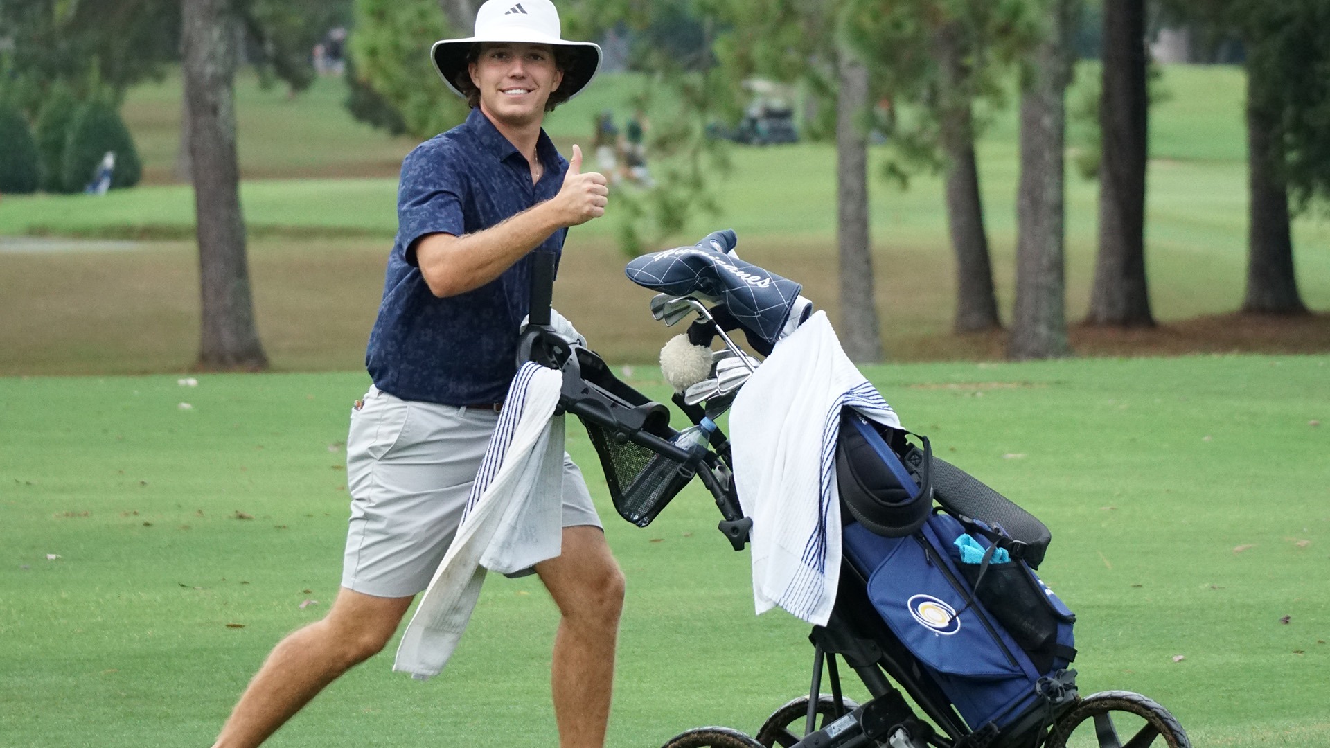 Sam Brown gives thumbs up while pushing clubs cart