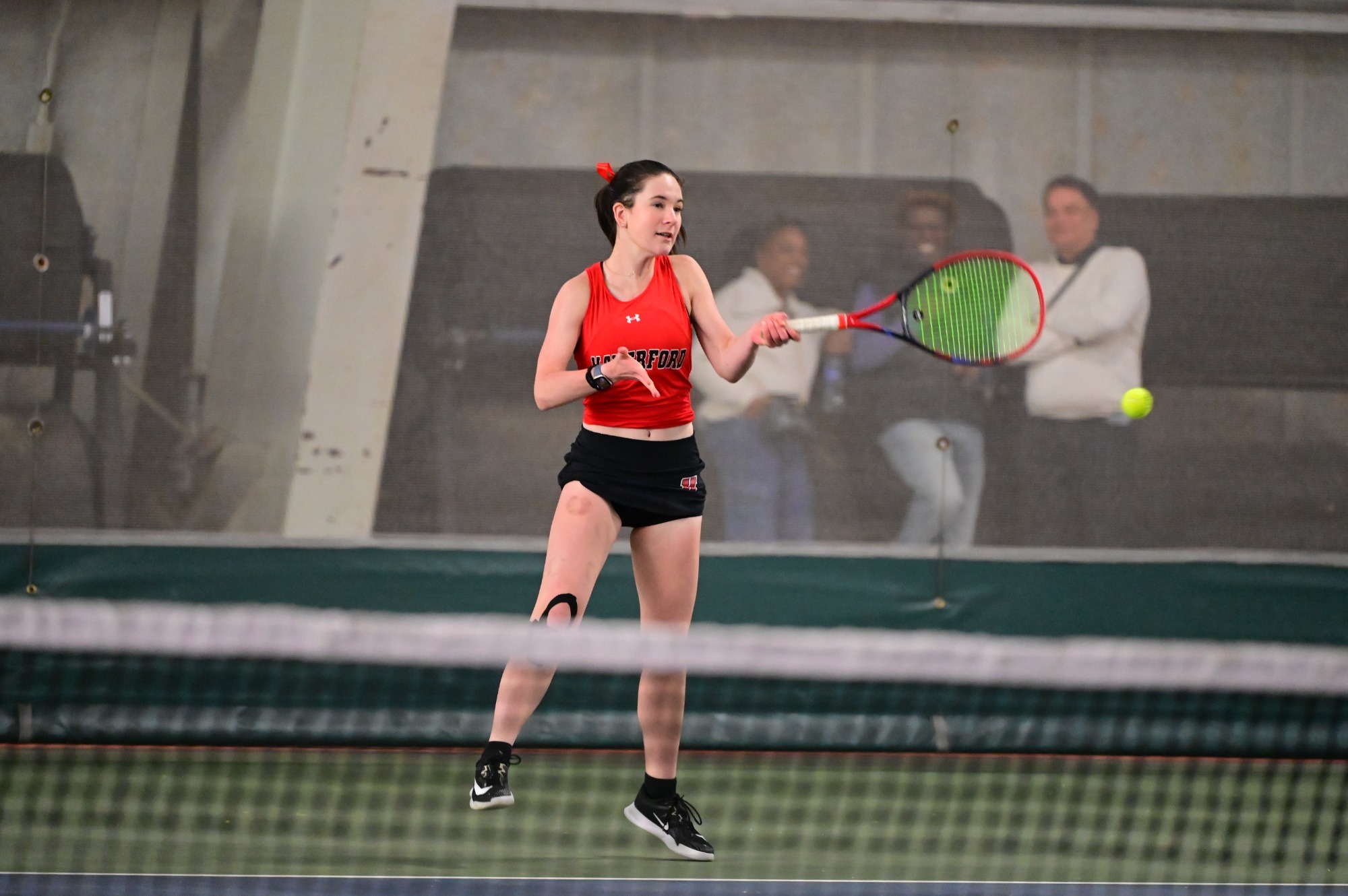 Haverford tennis player Adelaide Kreutel swings her racket during an indoor match, wearing a red tank top and black skirt.
