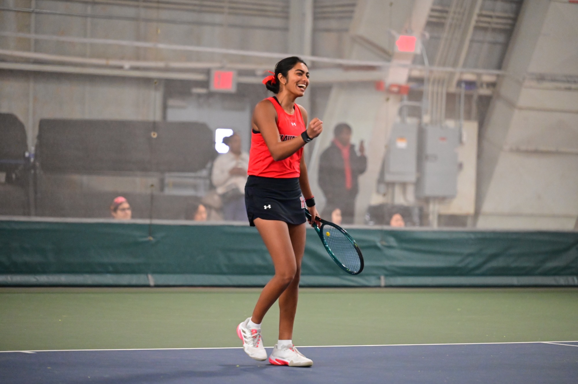 Abhi Menon, a smiling Haverford tennis player in a red jersey celebrates a point on an indoor tennis court.