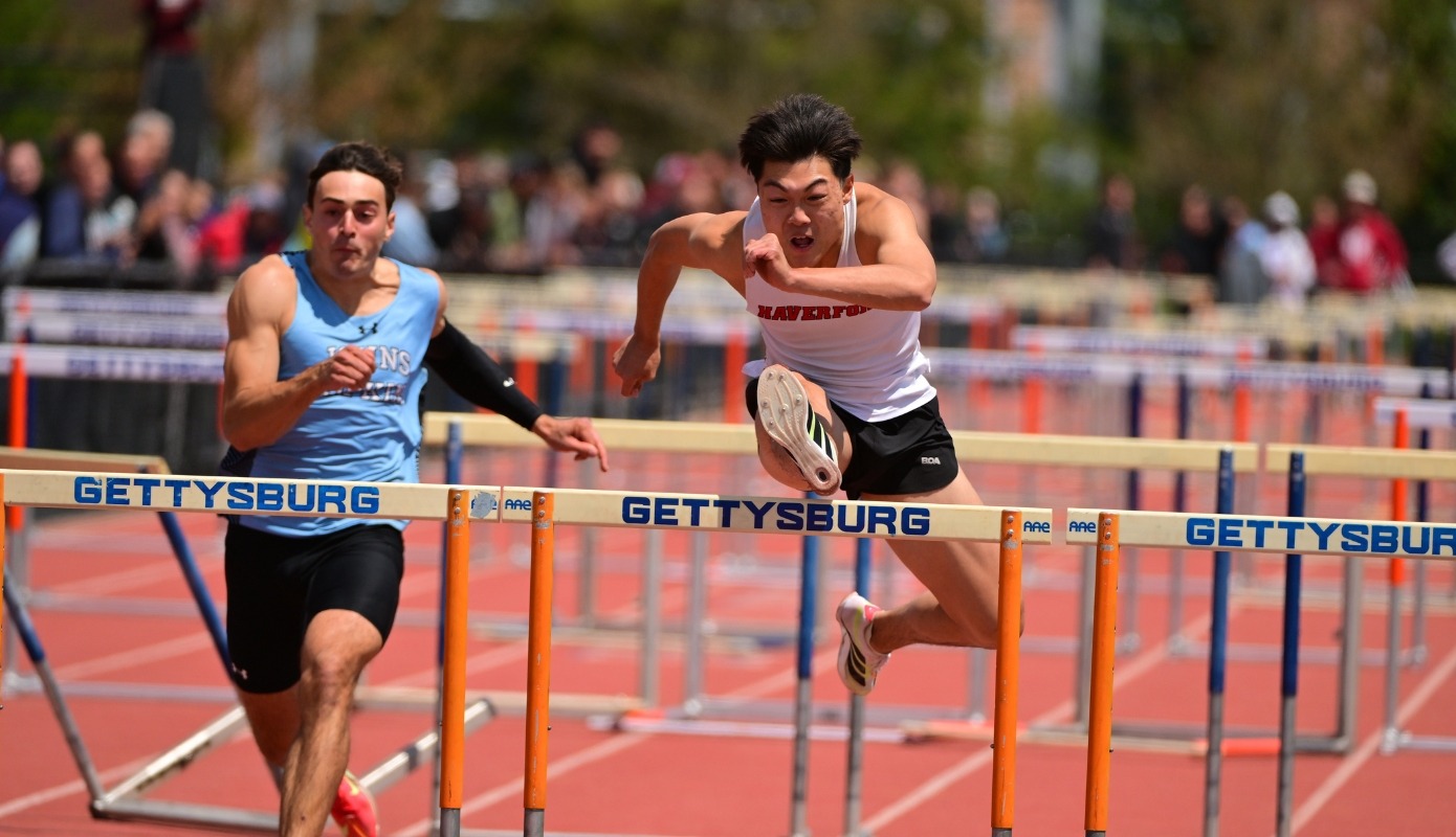 A Haverford student-athlete, Samuel Lin, clears a hurdle during a track and field competition at Gettysburg College, leading a runner from Johns Hopkins.