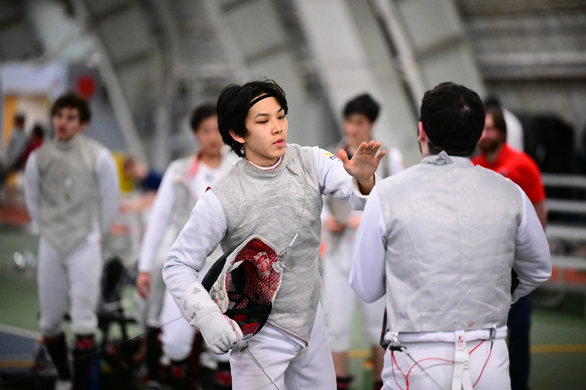 Oliver Po high fives a teammate in fencing gear inside Alumni Field House