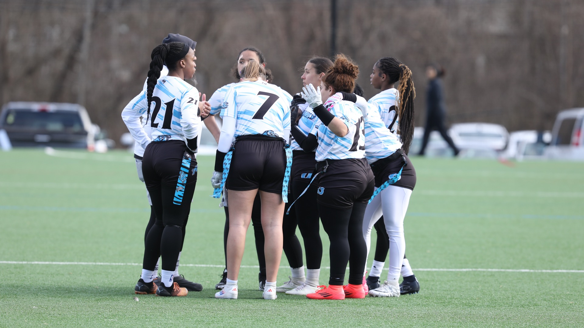 Wearing white uniforms and black shorts, the HFU flag football team huddles up on the field
